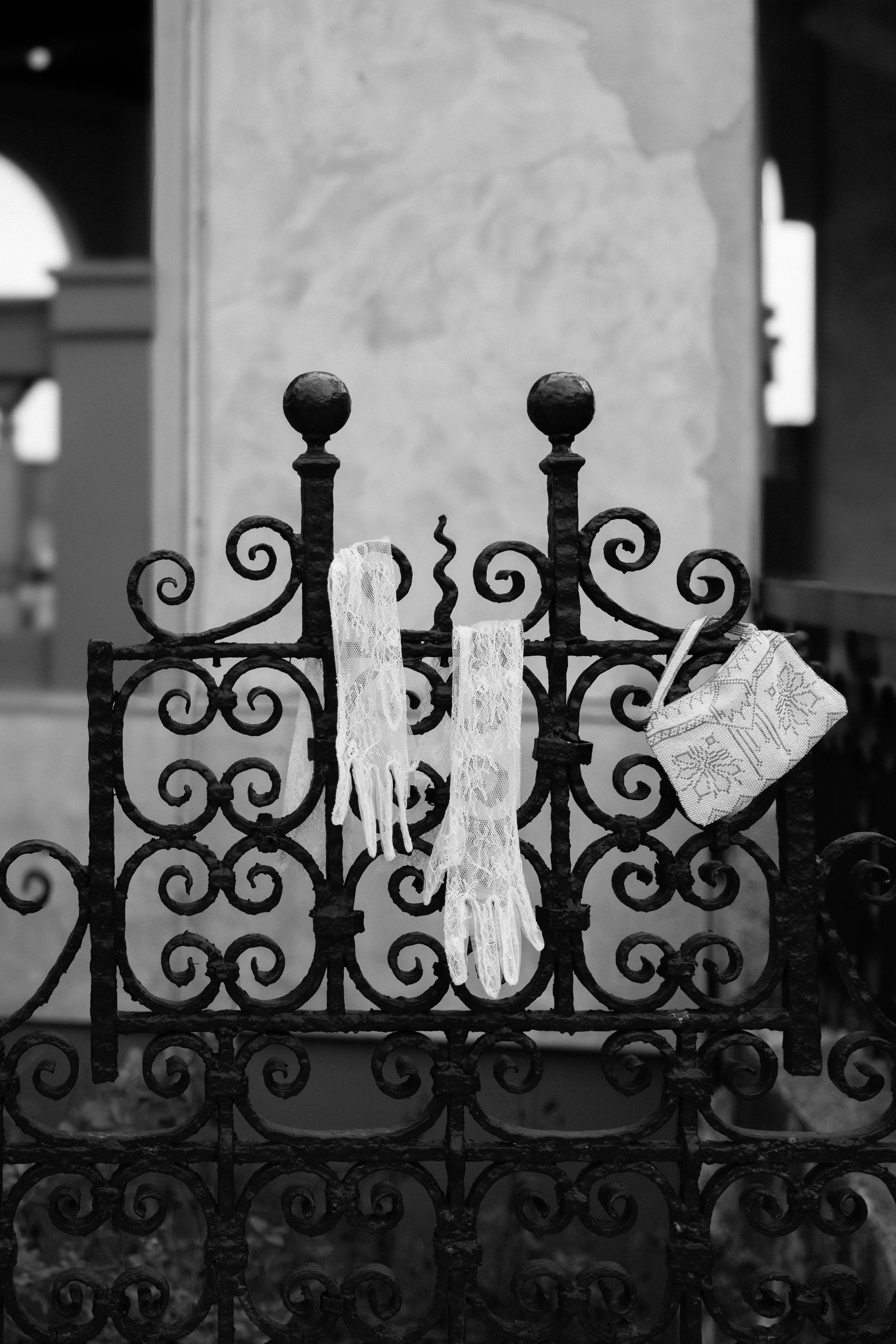 A black and white image of long lace gloves and a beaded purse hanging over a small iron gate.