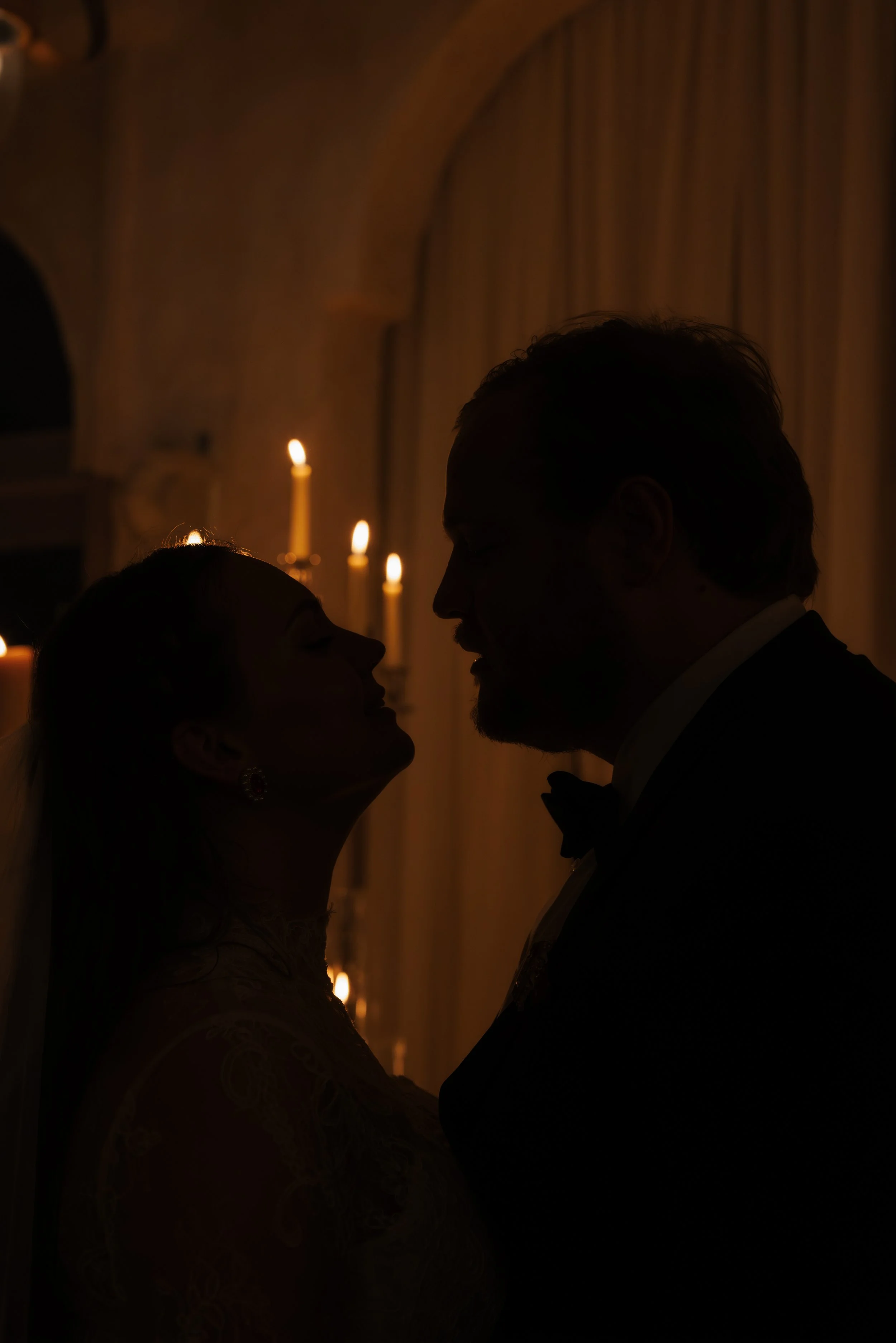 The silhouette of a man and woman going in for a kiss, backlit by candles.