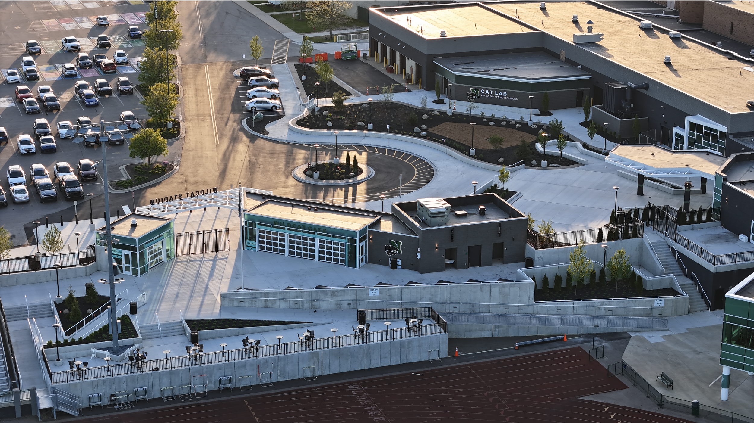 Aerial view of a modern school campus with parking lots, landscaped areas, a running track, and a building labeled 'Cat Lab' and 'Wildcat Cafe.'