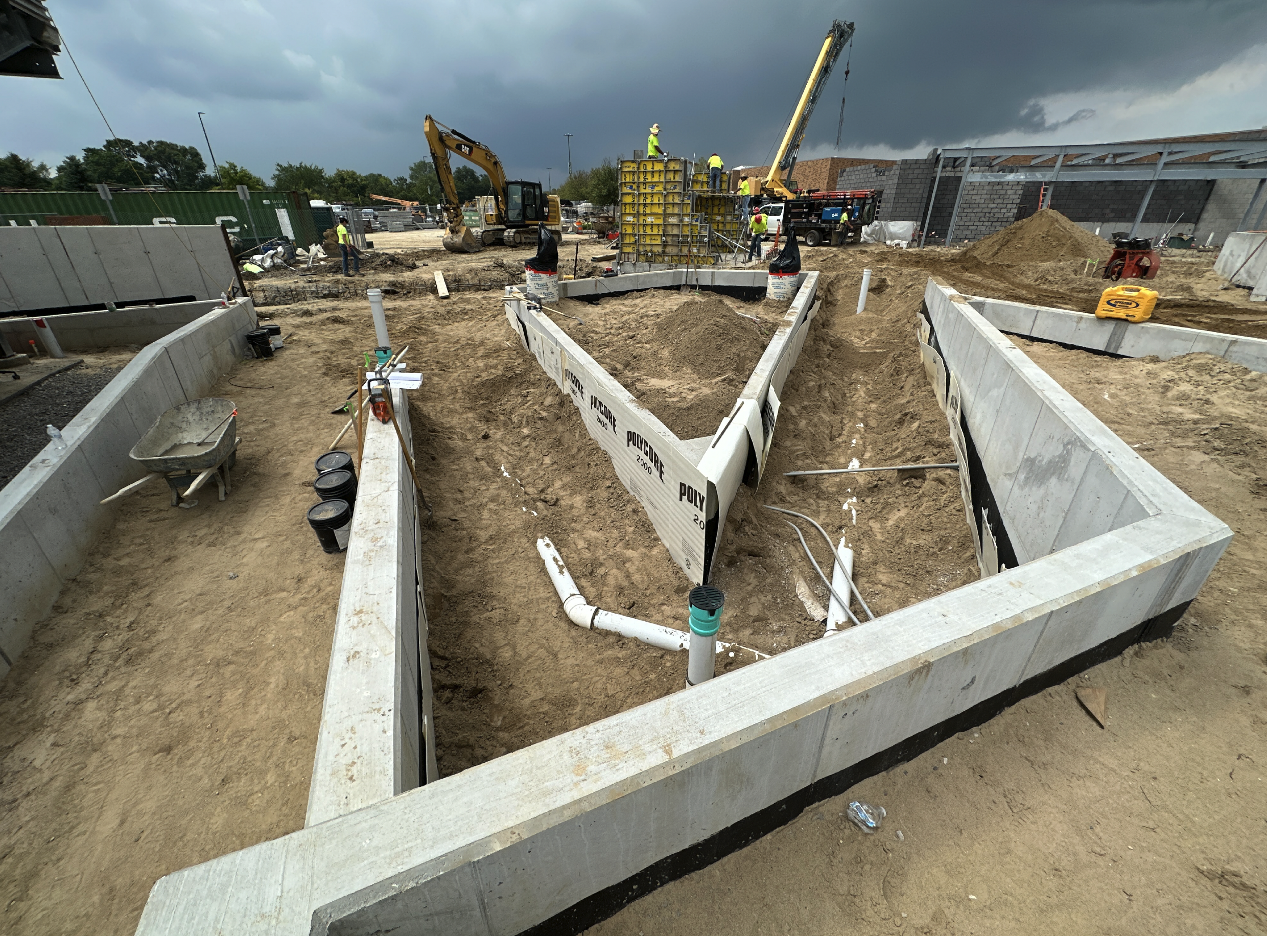 Construction site with concrete foundation, workers, and heavy machinery under a cloudy sky.