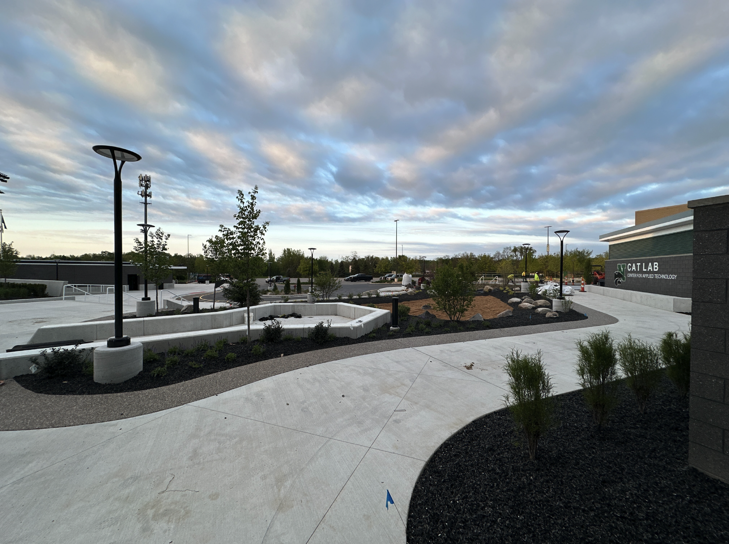 Modern outdoor campus area with paved walkways, landscaped garden beds, young trees, and street lamps. In the background, a building has a sign that reads 'CAT LAB' and 'CENTER FOR APPLIED TECHNOLOGY' with a paw print logo.