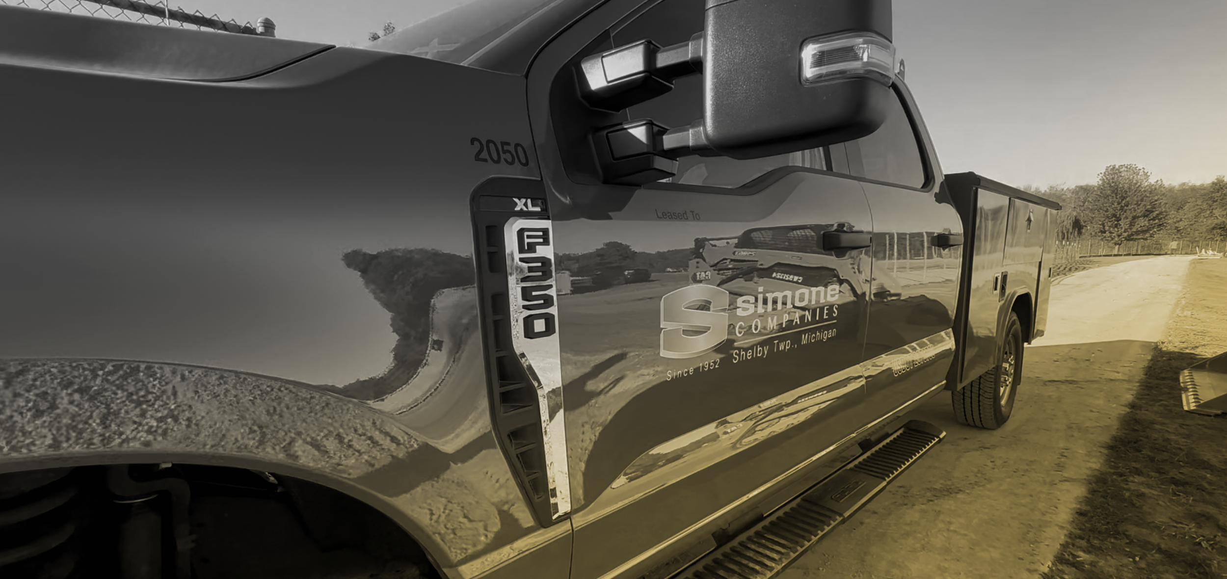 Black pickup truck with company logo and text on the side, parked on a dirt road with trees in the background.