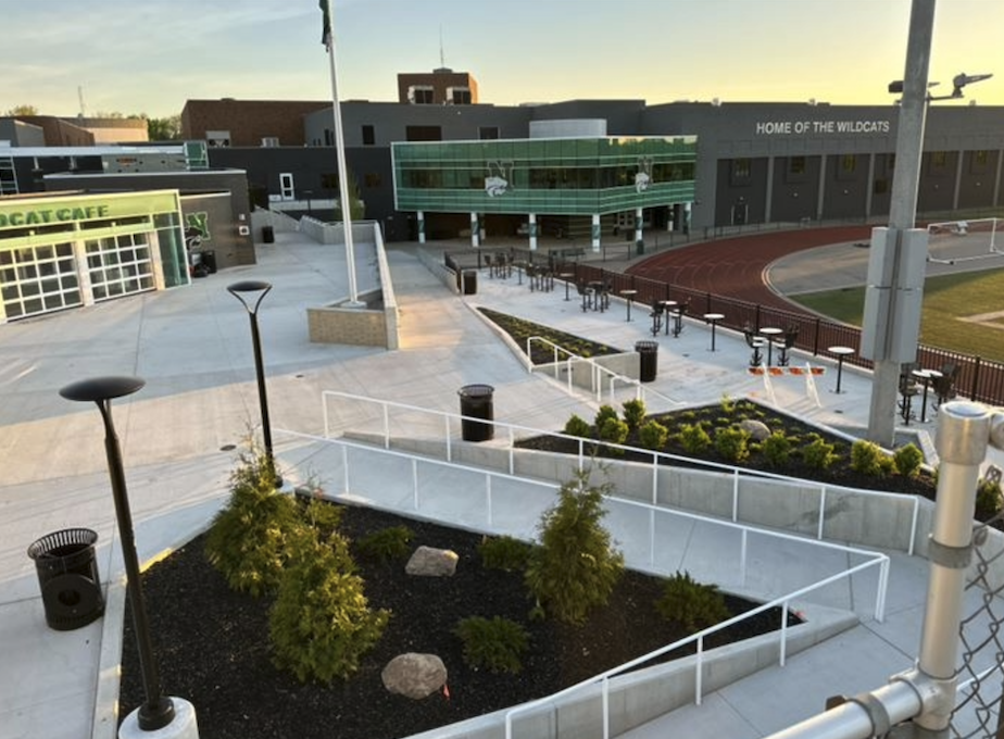Empty outdoor area at a school with trees, benches, and a track, featuring a building with a sign that reads 'HOME OF THE WILDCATS' in the background.