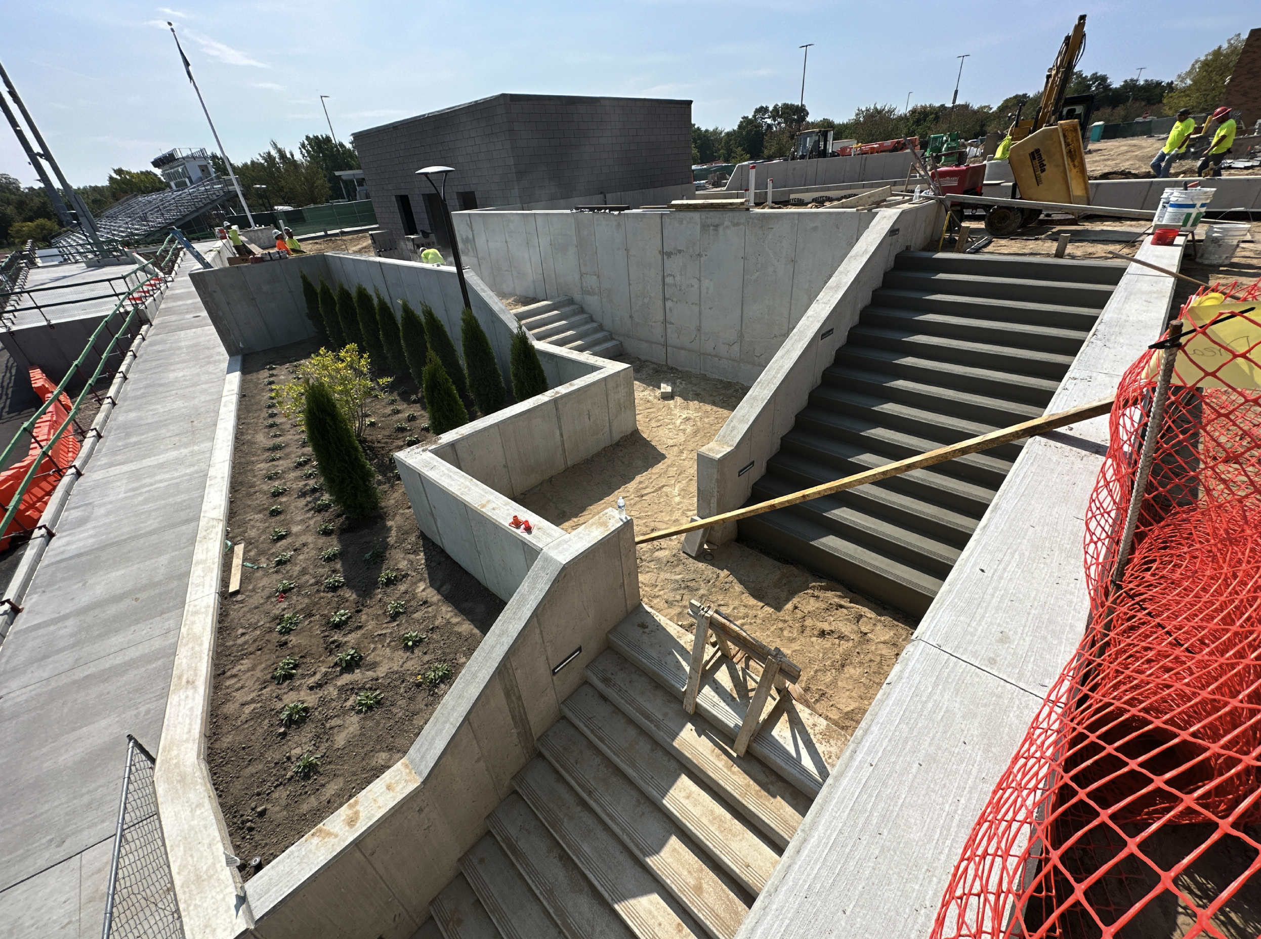 Construction site with concrete stairs, landscaping, and workers installing infrastructure.