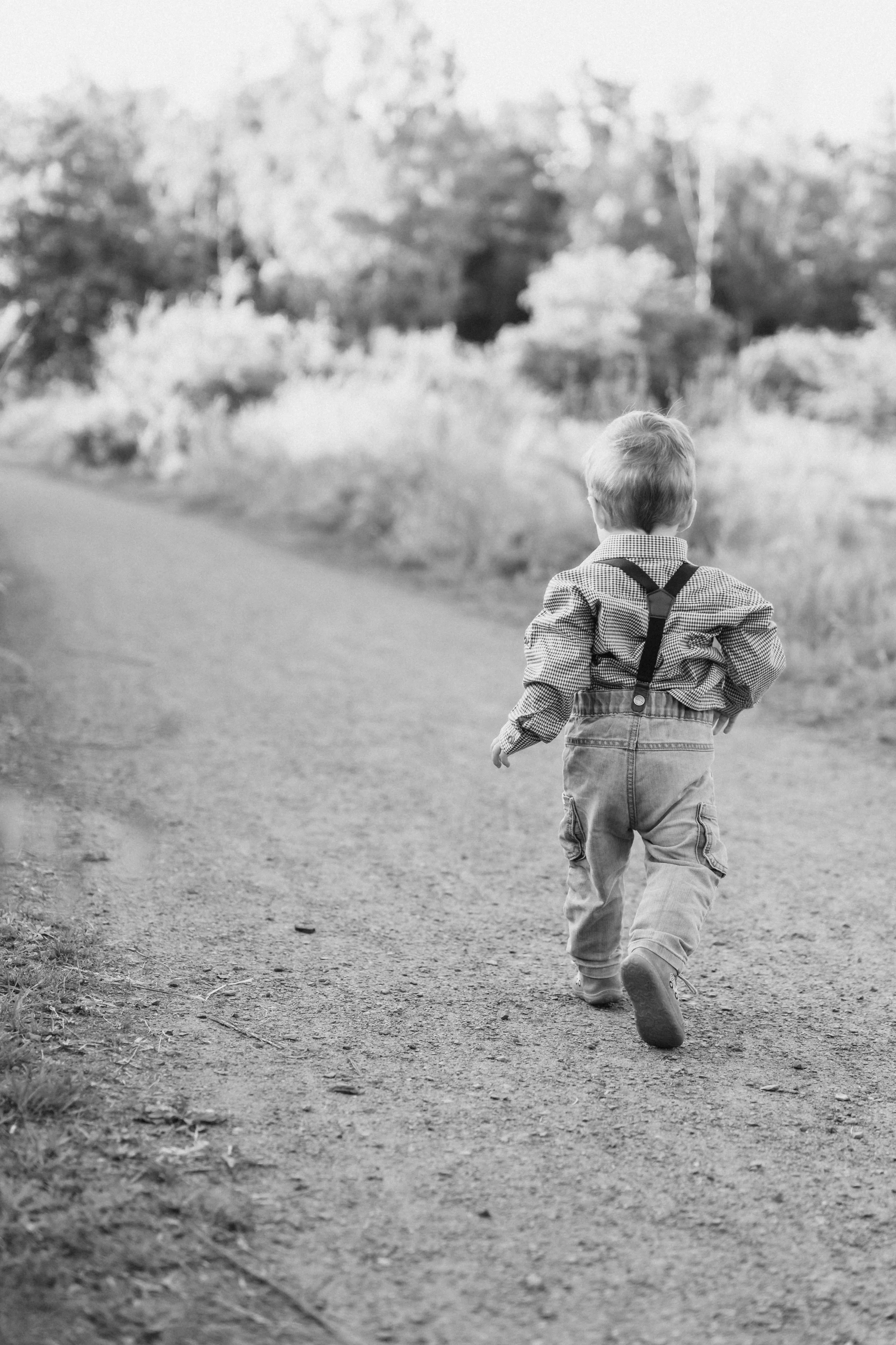 Junger Junge läuft auf einem Weg, Rückenansicht, in einer natürlichen Umgebung mit Bäumen und Büschen, schwarz-weiß Fotografien.