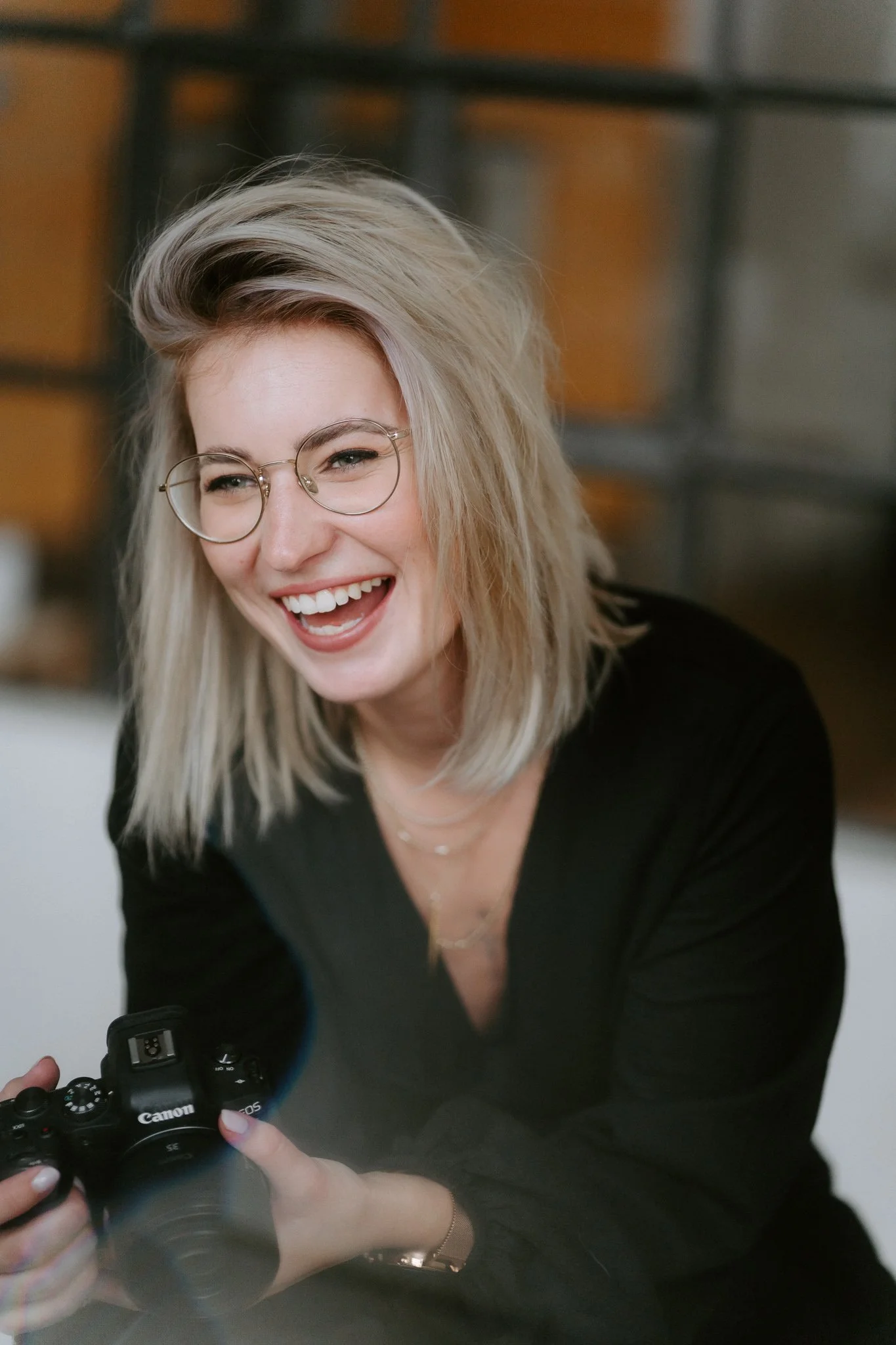 Lächelnde Frau mit Brille hält eine Canon Kamera.