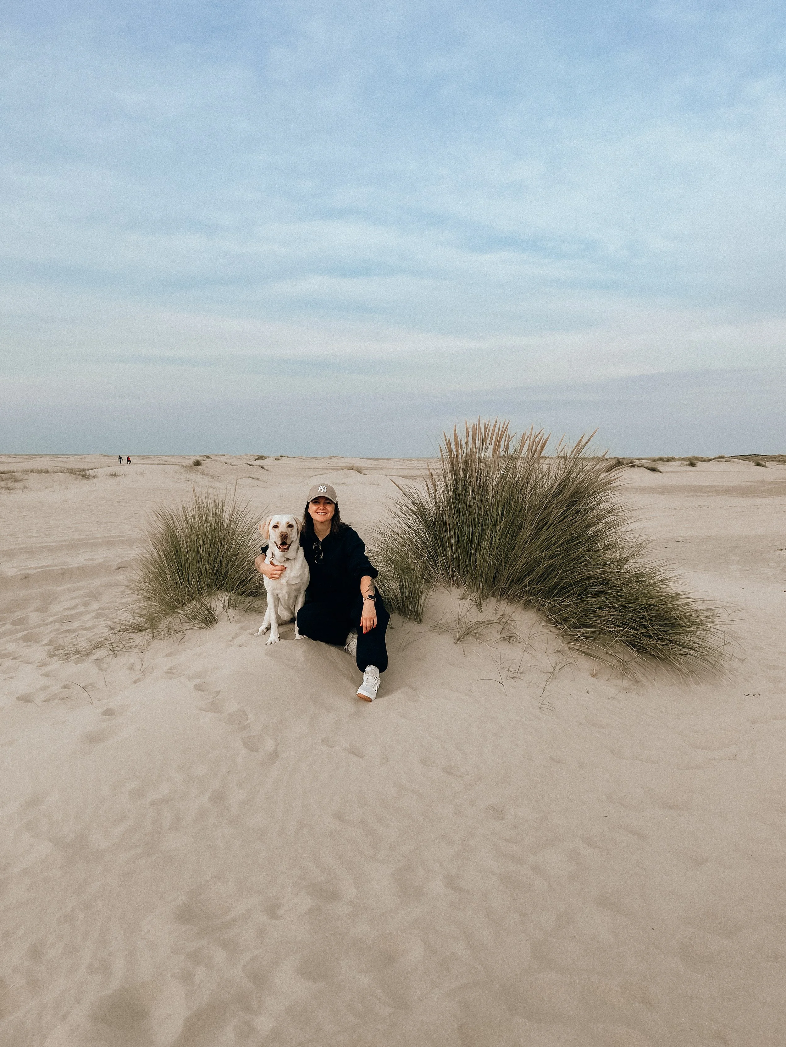 Eine Frau sitzt mit ihrem Labrador in den Dünen Zeelands