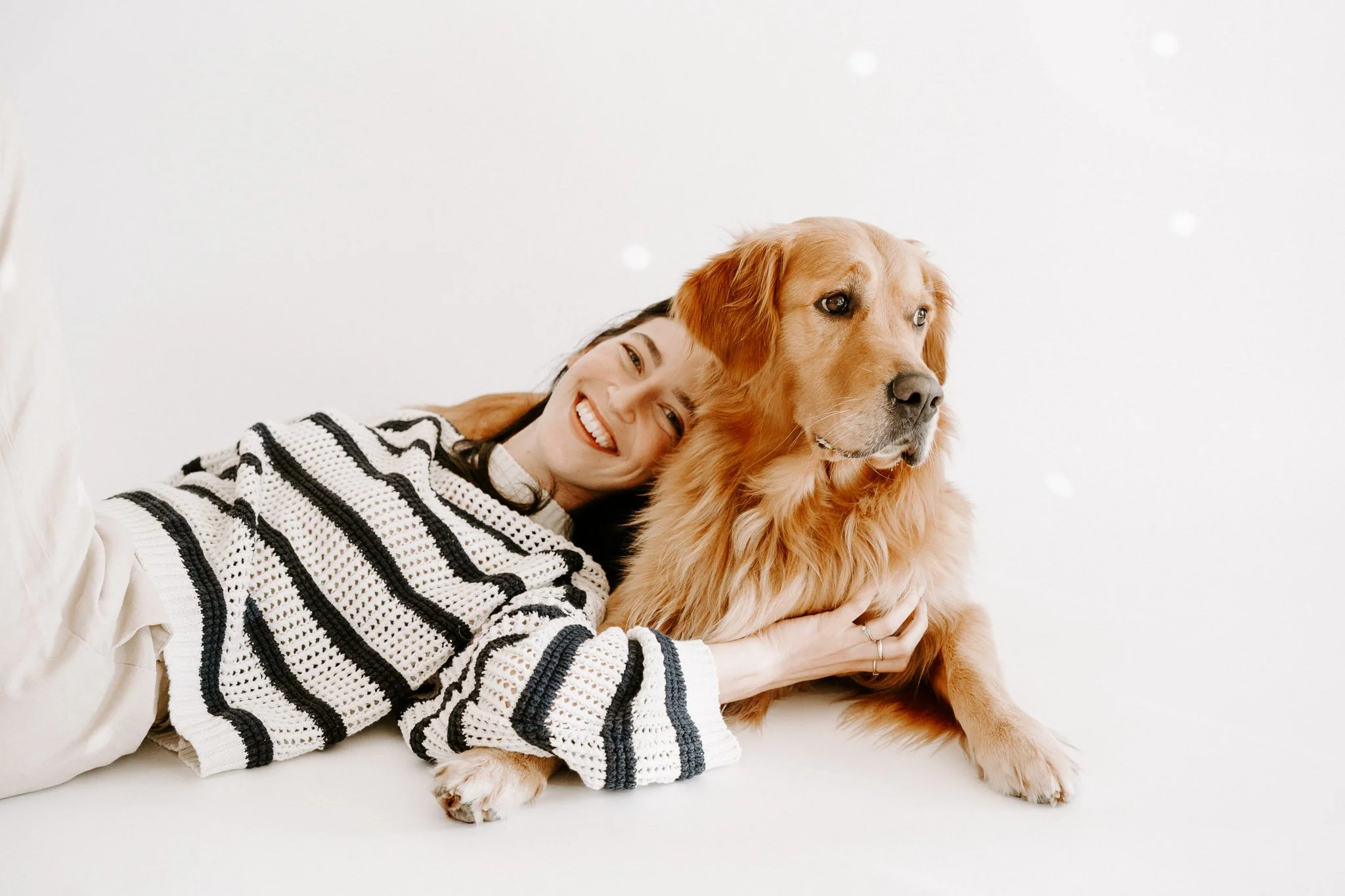 Eine lachende Frau liegt neben einem goldenen Retriever-Hund auf einem weißen Hintergrund.