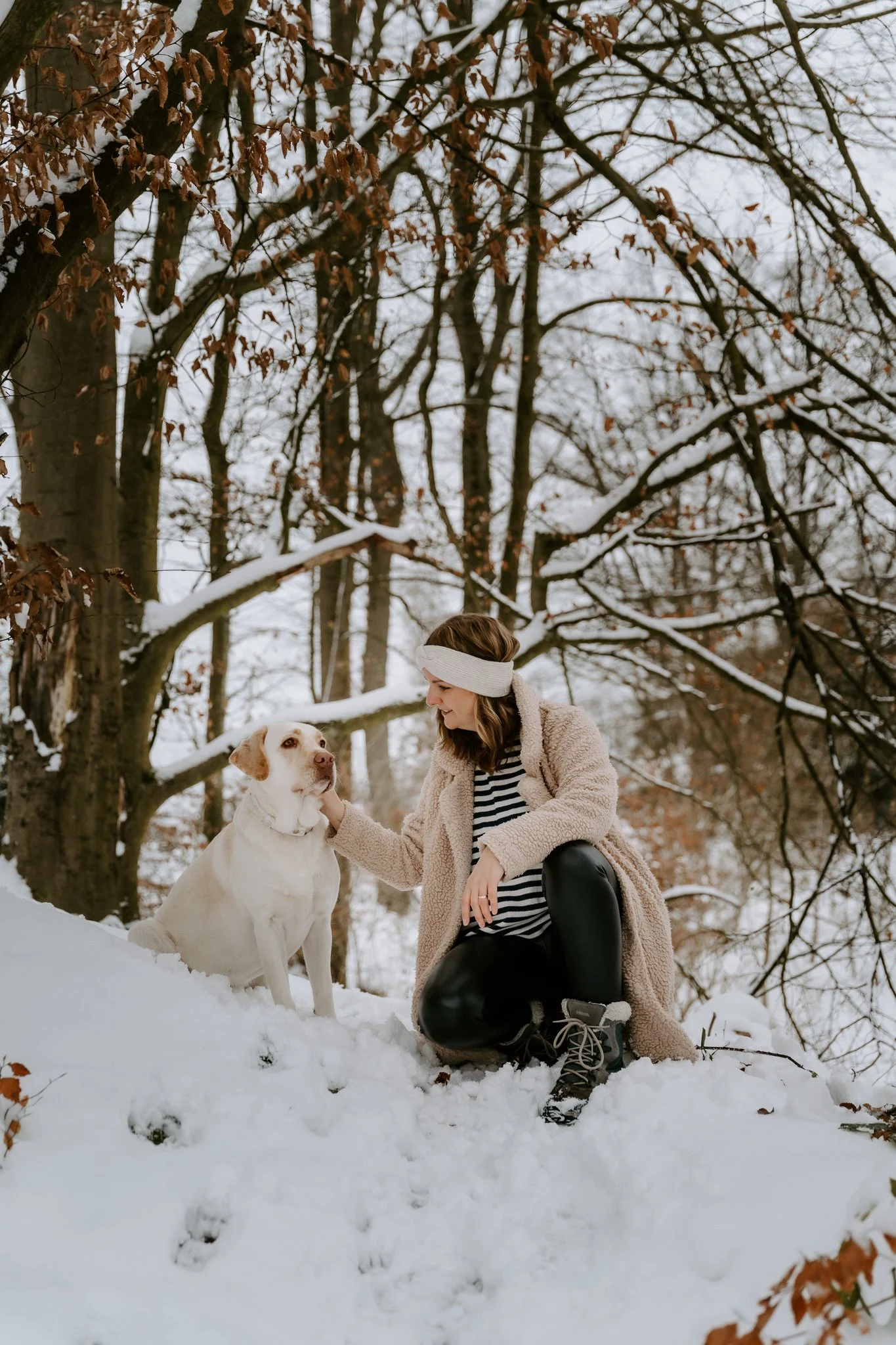Frau mit Hund im verschneiten Wald unterwegs