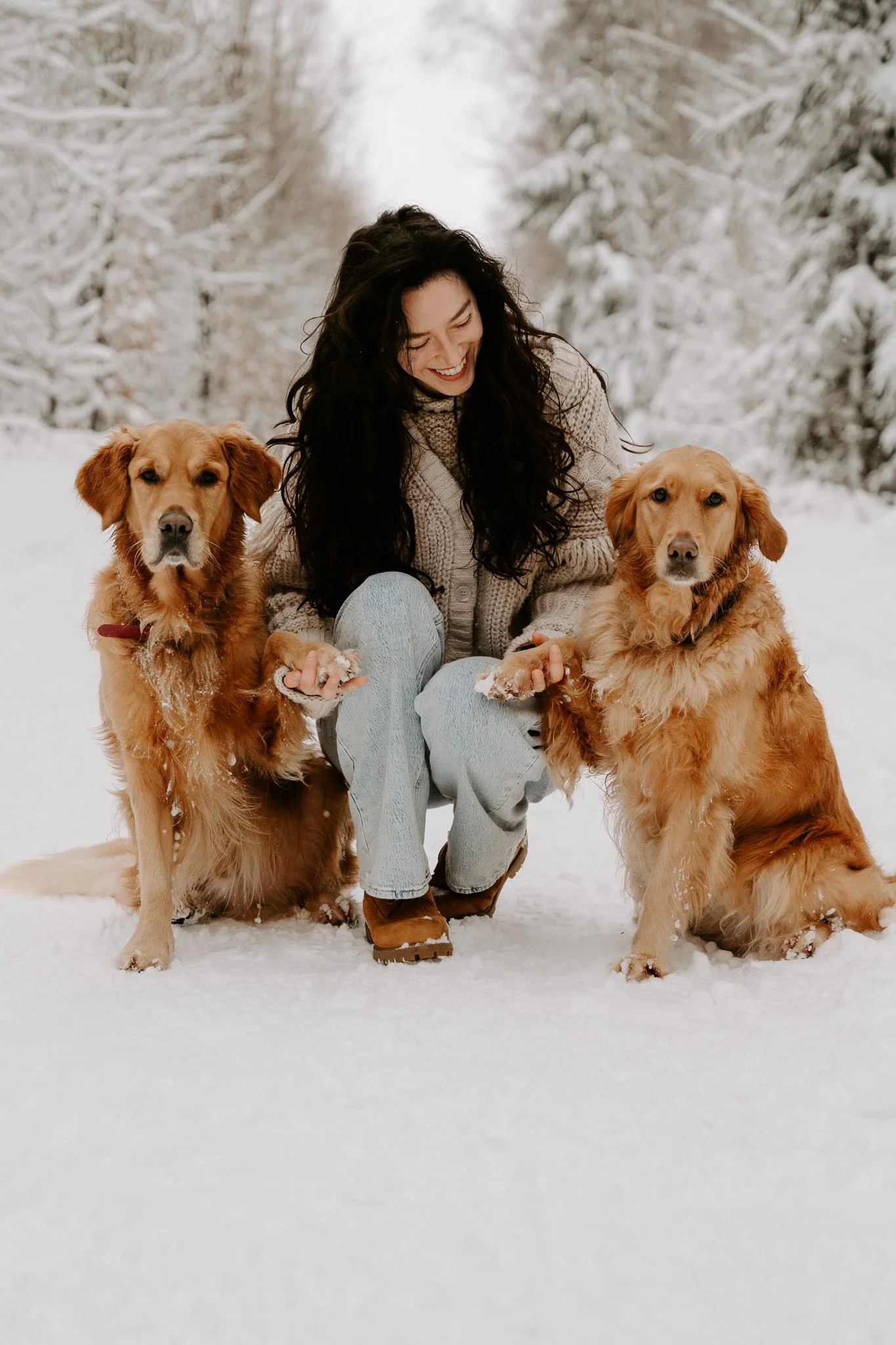 Frau mit zwei Golden Retrievern in verschneiter Landschaft, lachend.