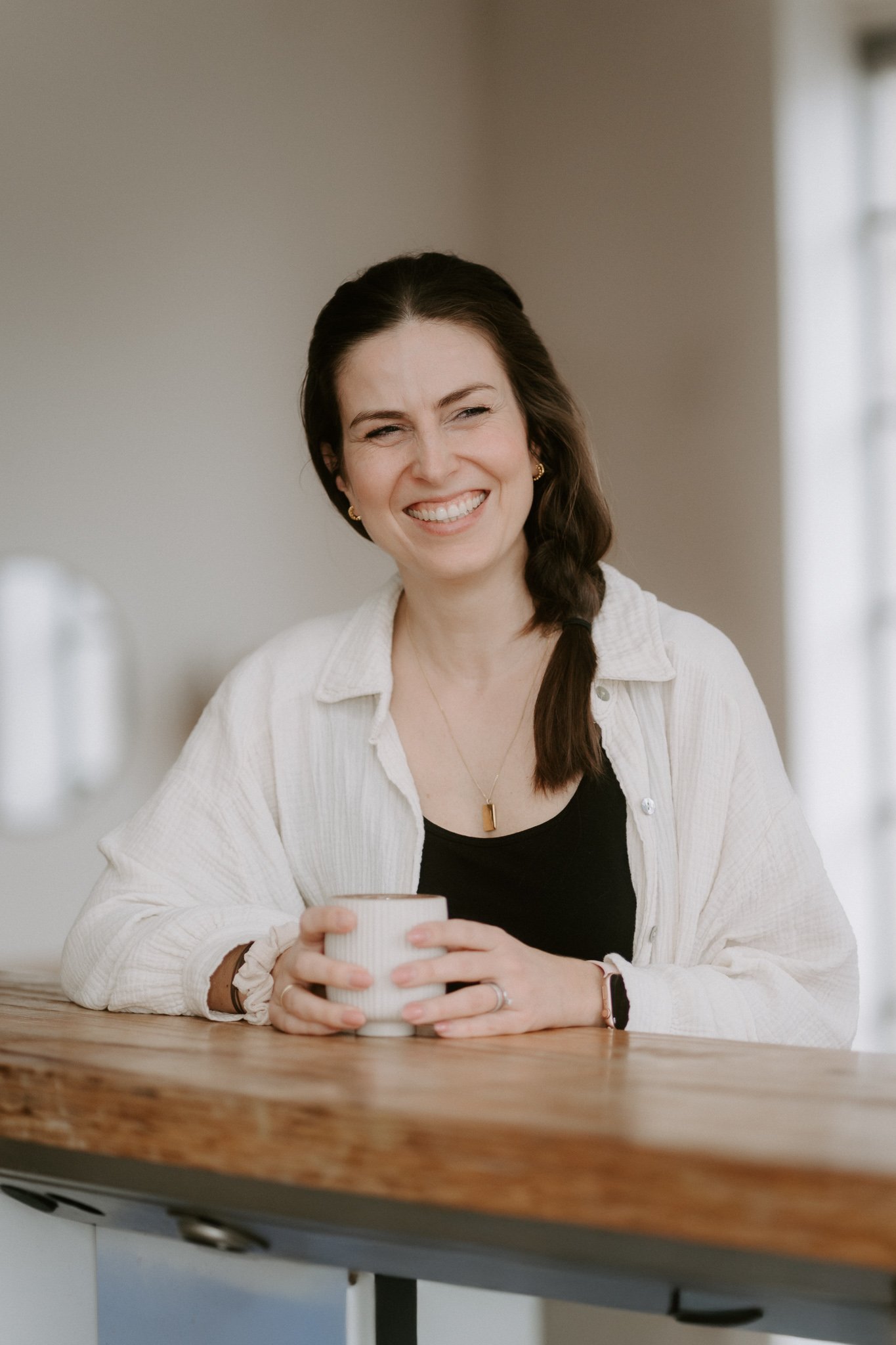 Junge Frau steht mit ihrem Kaffee an einer Theke, indoor