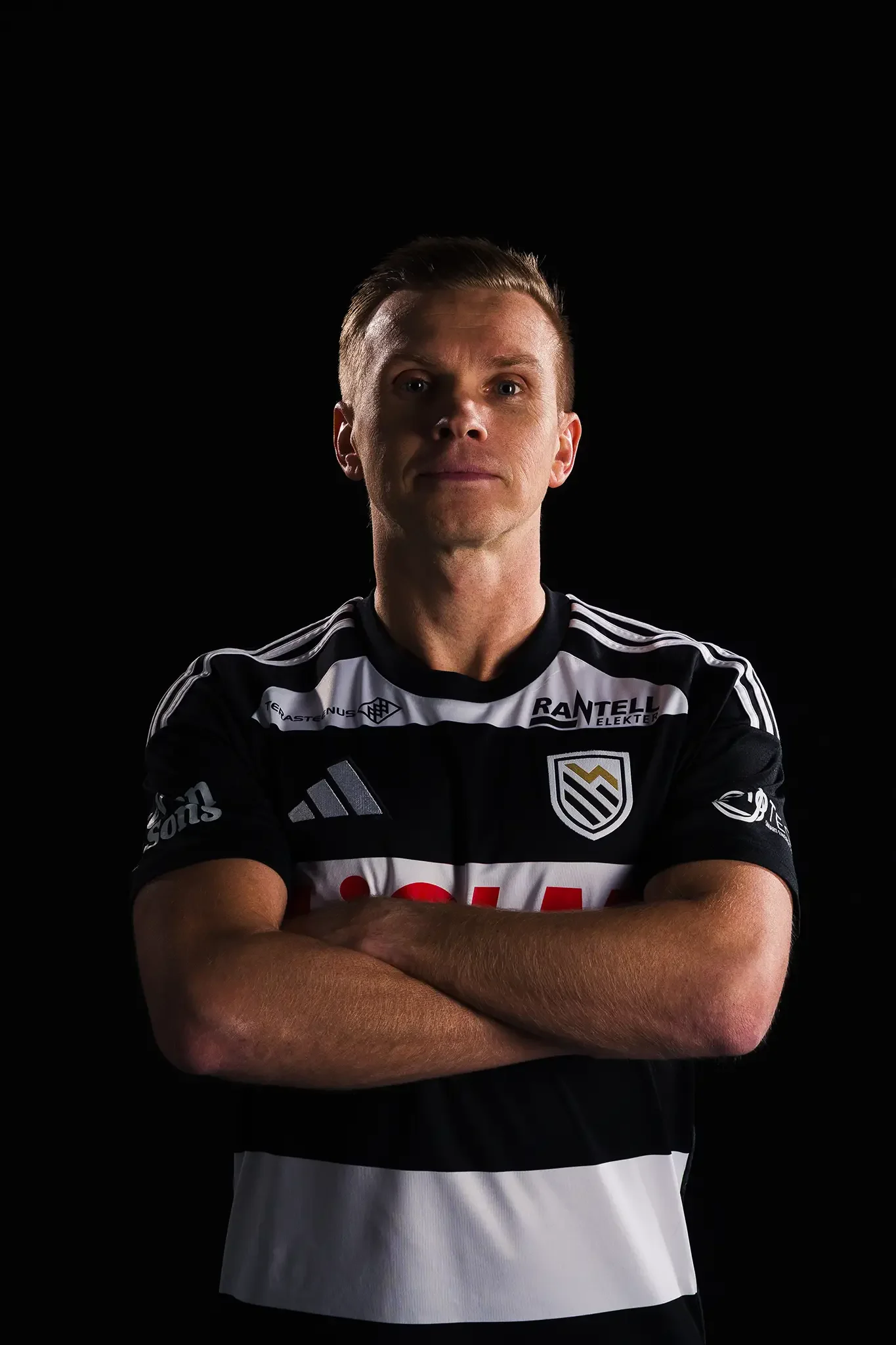 ametiportree Tartu JK Welco kapten Taijo Tenistest poseerib stuudios tumedal taustal käed risti jalgpalliklubisärgis enesekindlalt meediapäeval