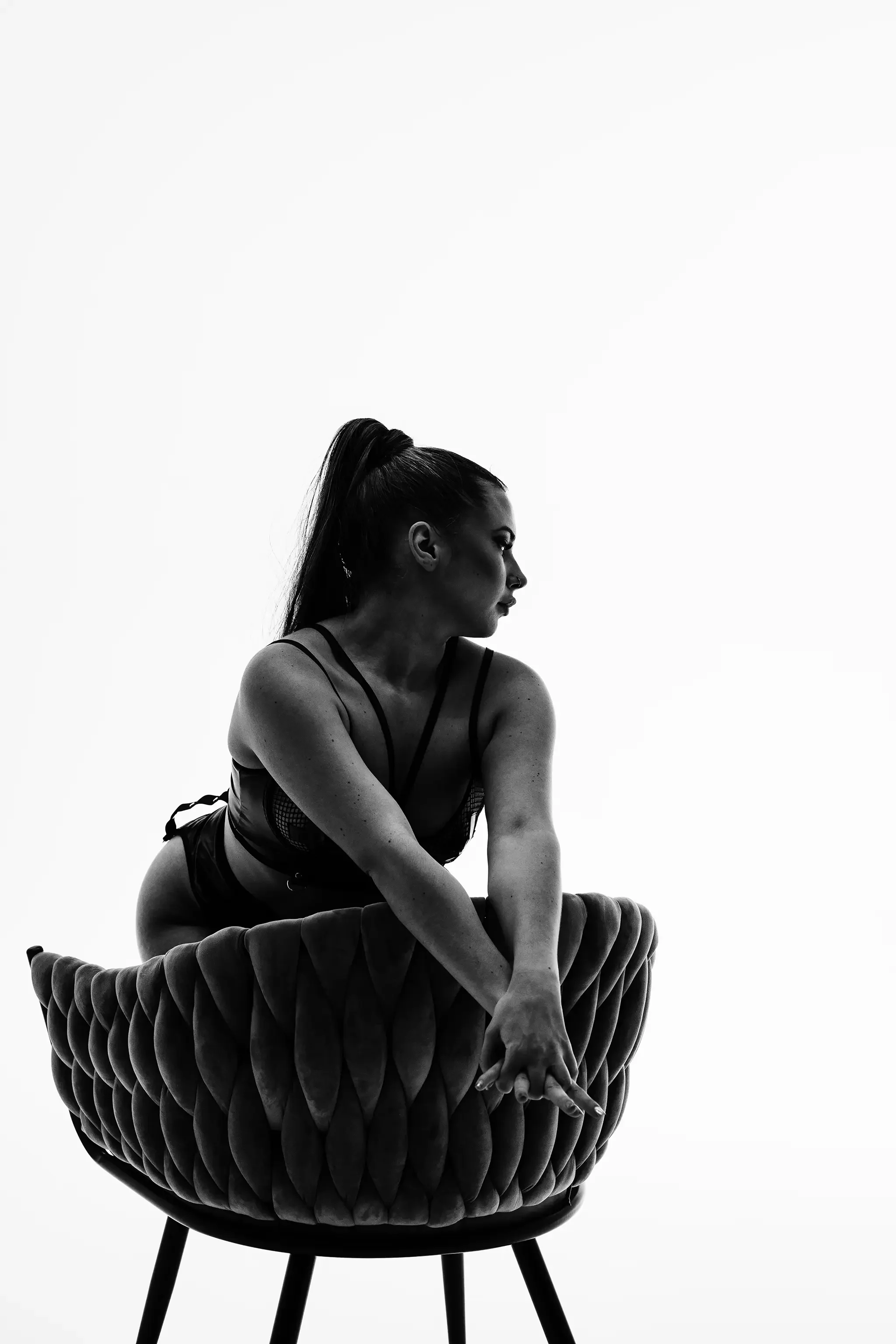 naine poseerib boudoir stiilis stuudioportreel heledas fotostuudios tugitoolil vaadates elegantselt ja enesekindlalt küljele