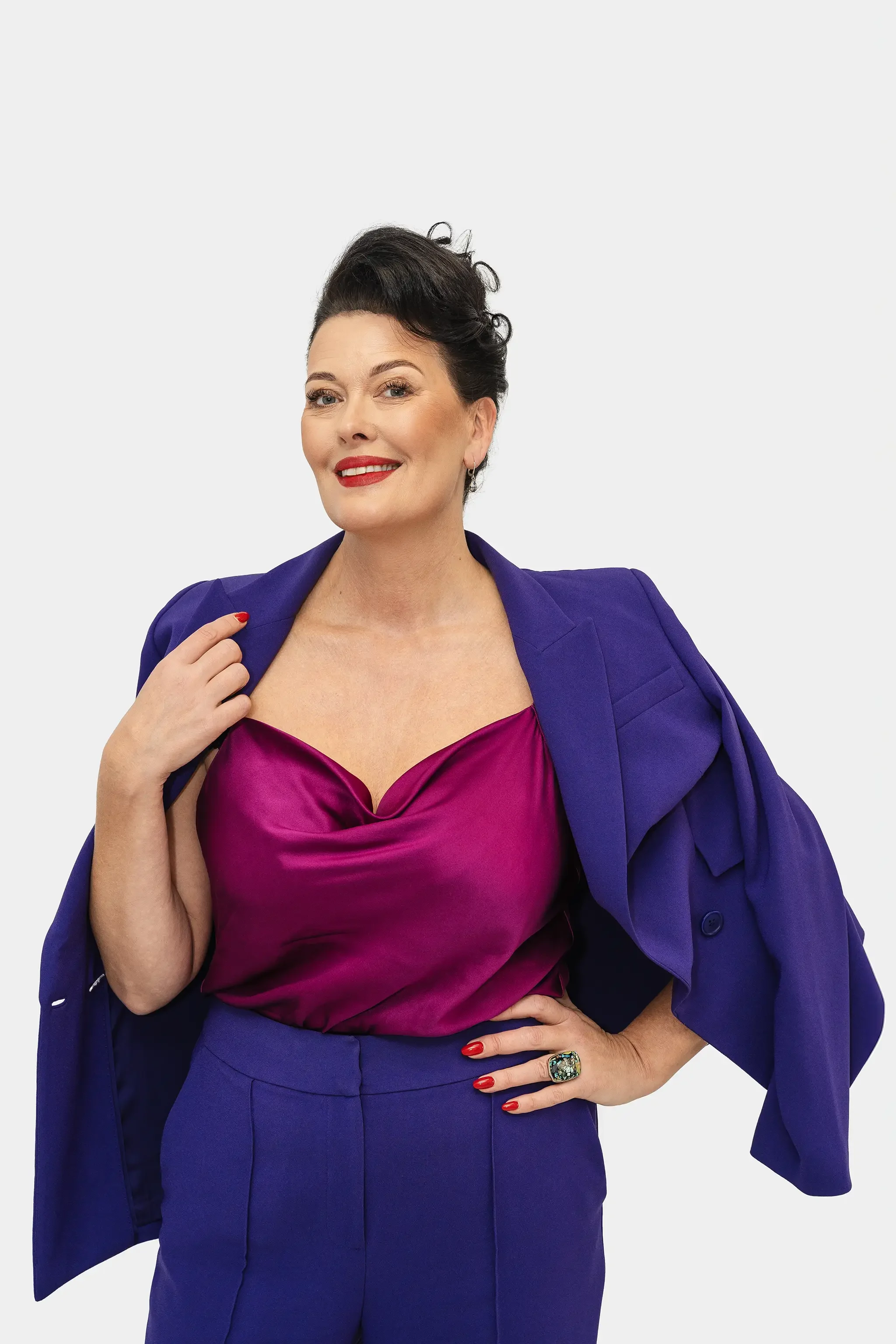 Merle Palmiste poseerib stuudios valgel taustal portreepildistamisel violetse pintsaku ja magenta topiga naeratades enesekindla ja elegantse meeleoluga brändifoto jaoks