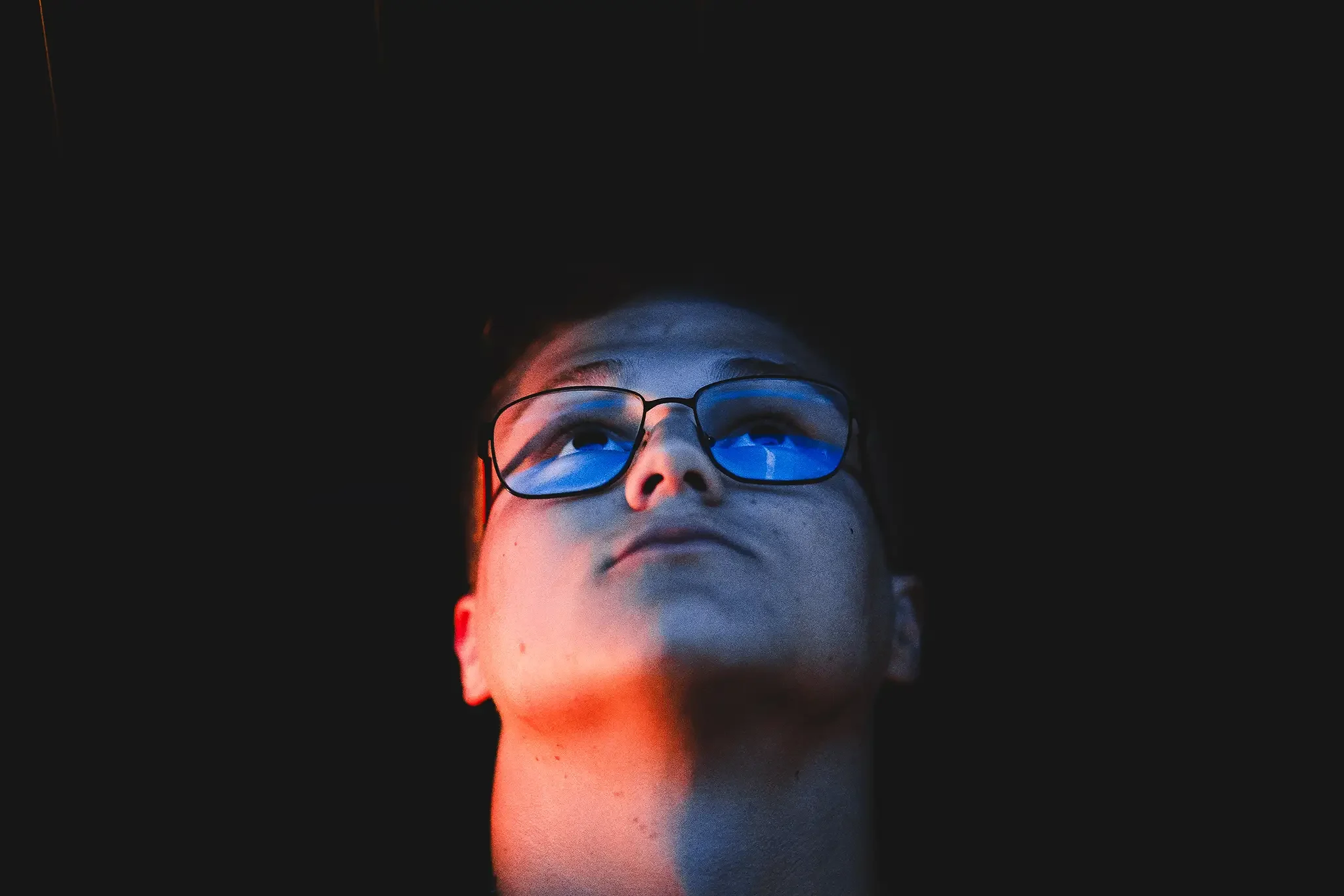 portree lähivõte tartu aparaaditehases prillidega noormehest vaadates üles tumedas ruumis sinise ja oranži valgusega
