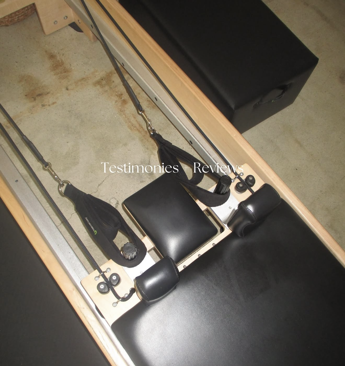 A Pilates reformer machine with adjustable straps and padded supports on a concrete floor.