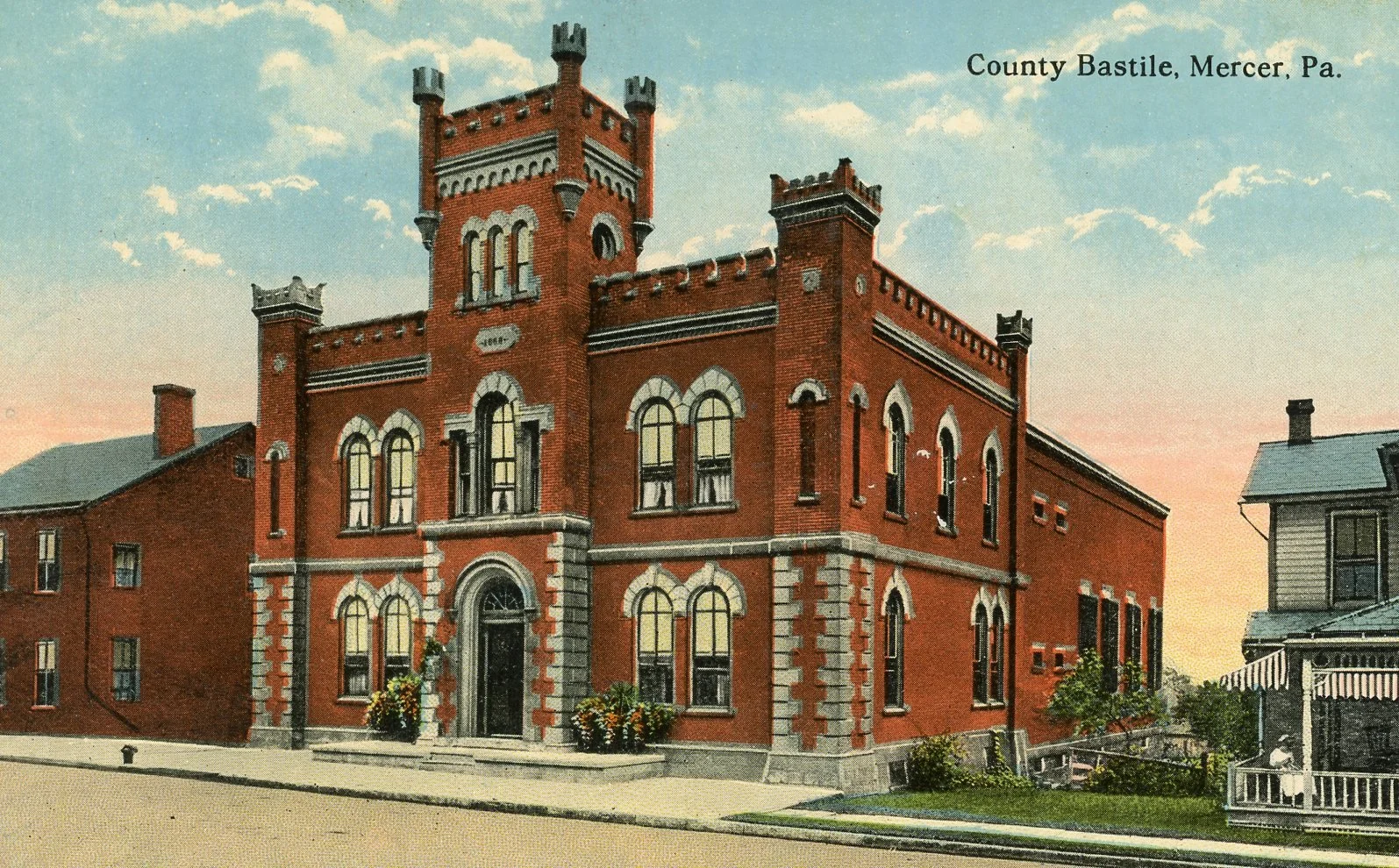 Historic red brick County Bastile building in Mercer, Pennsylvania, with a tower, arched windows, and decorative stone accents, set against a sky with clouds.