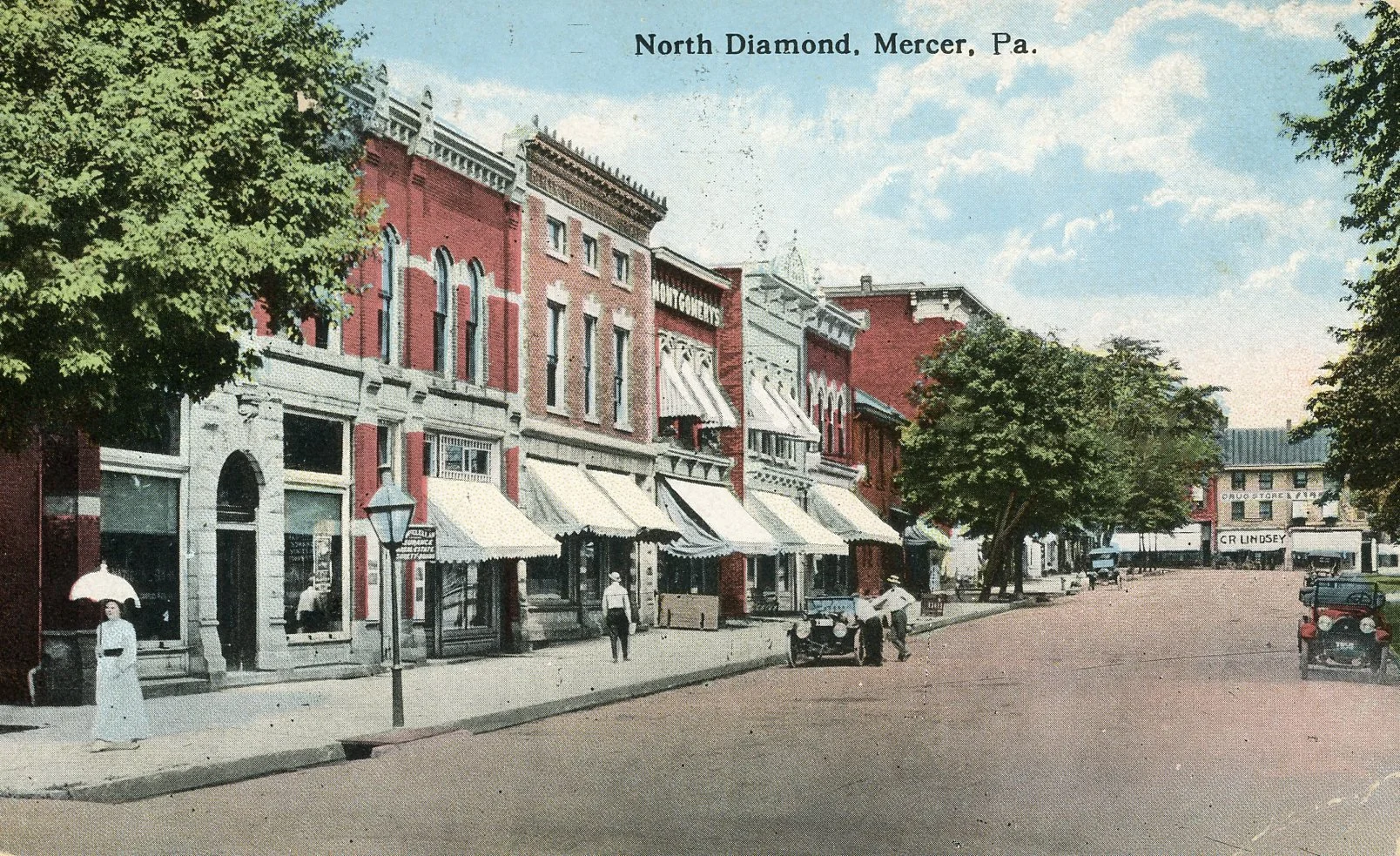 Vintage photograph of North Diamond street in Mercer, Pennsylvania, showing storefronts with awnings, trees lining the street, and early 20th-century cars parked along the roadside.