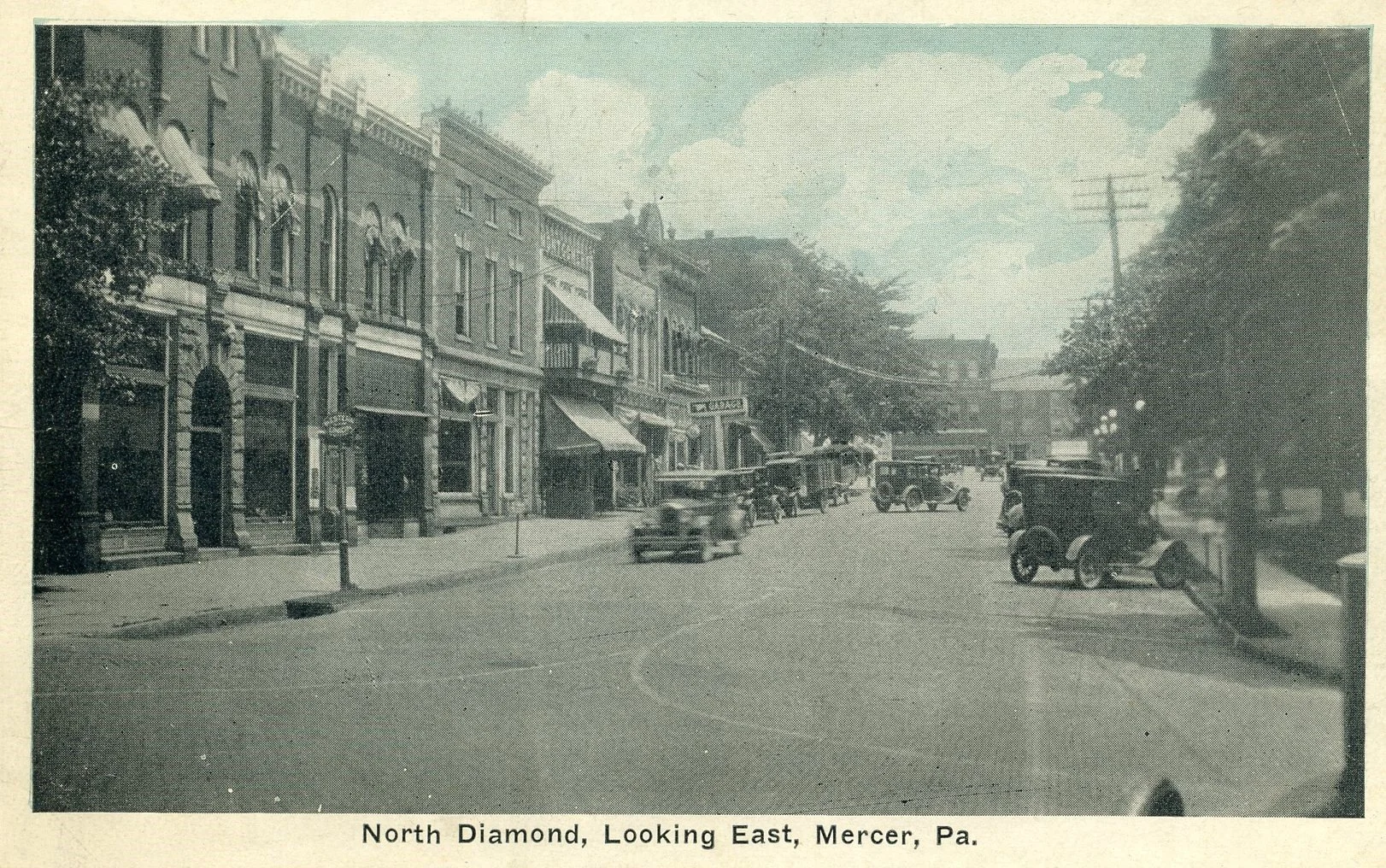 A black and white photo of North Diamond street looking east in Mercer, Pennsylvania, showing vintage cars, trees, and historic buildings with storefronts from an early 20th-century era.