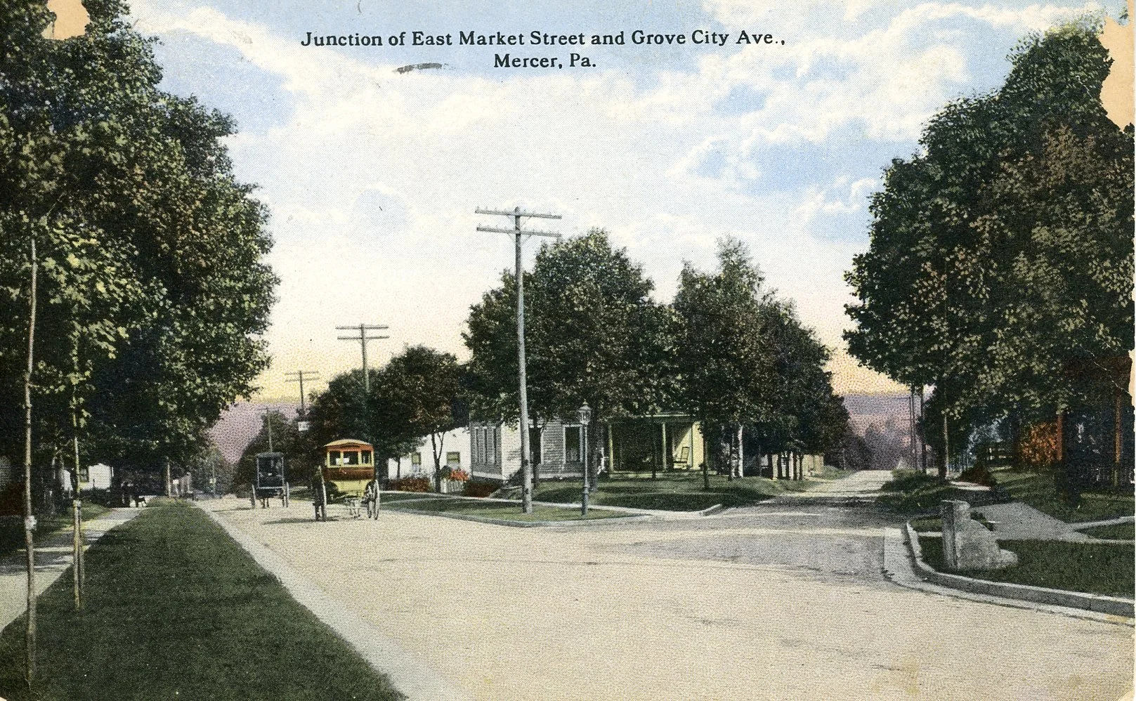 A historic black-and-white photograph of the intersection of East Market Street and Grove City Avenue in Mercer, Pennsylvania, with a horse-drawn trolley on the street, trees lining the sidewalks, and early 20th-century buildings.