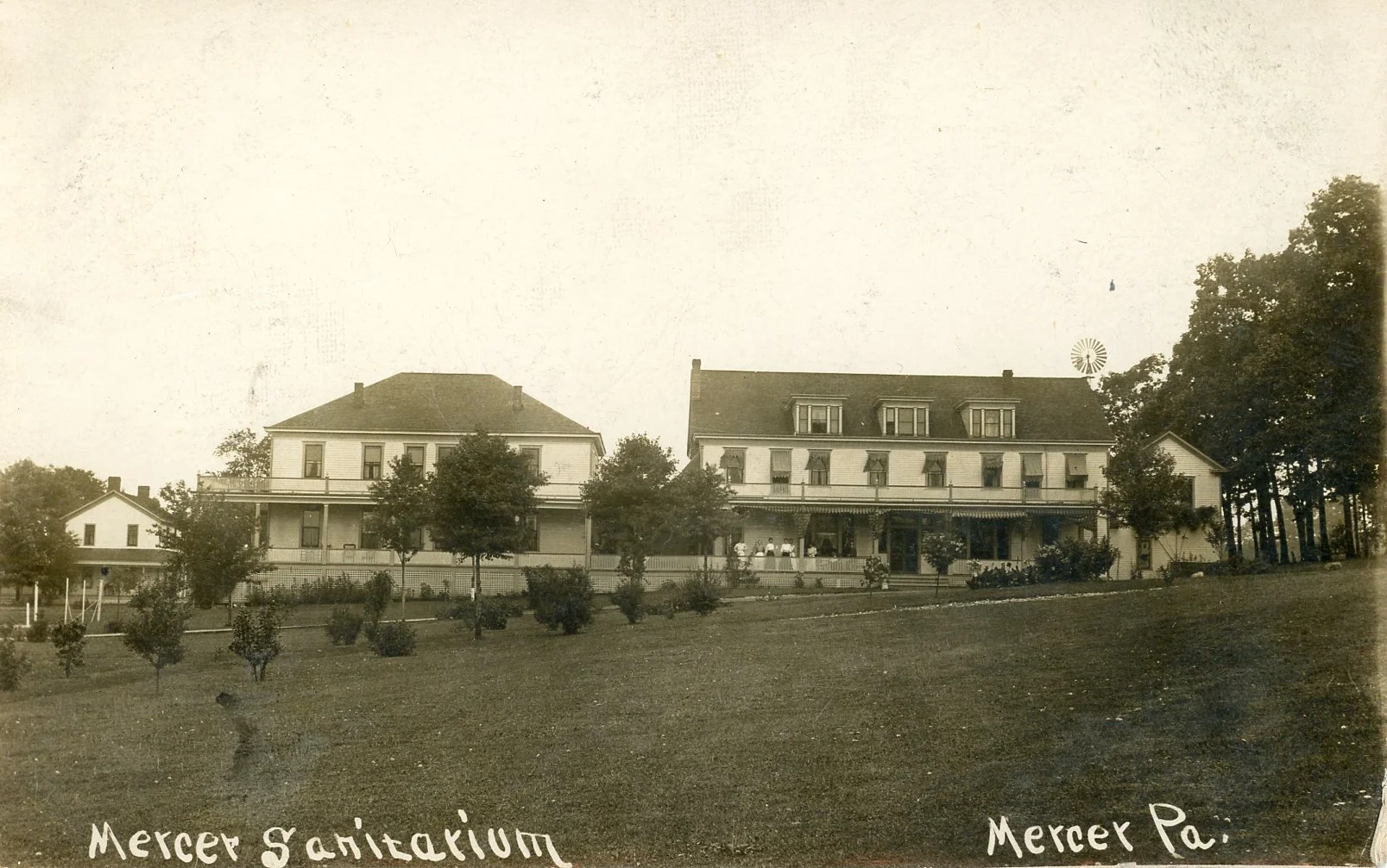 Old sepia-toned photograph of a large house with multiple windows and a porch, surrounded by trees and a grassy lawn, labeled 'Mercer Sanitarium' and 'Mercer Pa.'