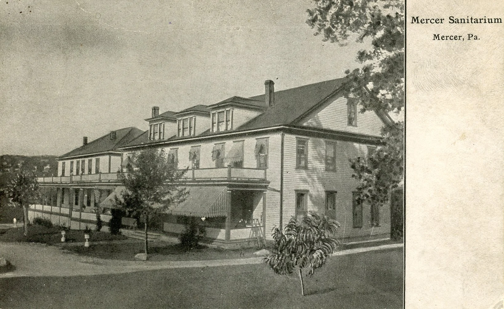 Old black and white photograph of Mercer Sanitarium in Mercer, Pennsylvania, showing a large, multi-story wooden building with a porch, trees, and a well-kept yard.