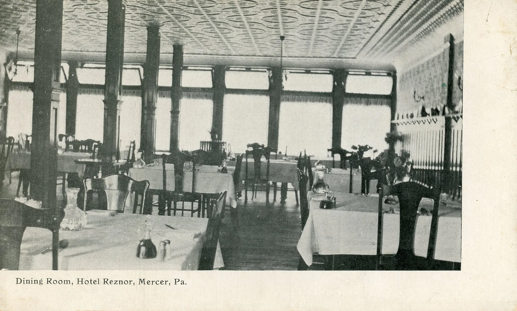 A black and white photograph of a dining room at Hotel Reznor in Mercer, Pennsylvania, with several tables set with tablecloths and chairs arranged around them.