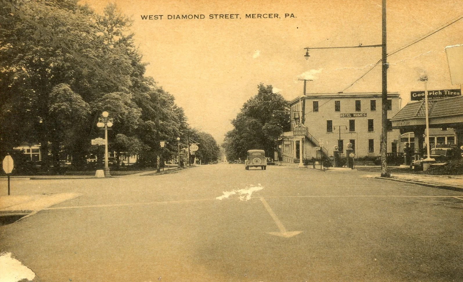 A vintage black-and-white photograph of West Diamond Street in Mercer, Pennsylvania, showing a quiet street lined with large trees, vintage street lamps, small shops, and a hotel named Hotel Humes with a sign for Sterling Gasoline. An old car is driv