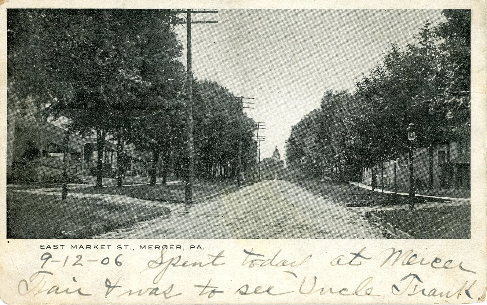 Historic black-and-white photograph of East Market Street in Mercer, Pennsylvania, showing a tree-lined street with utility poles and buildings on both sides, leading to a domed building or courthouse in the distance.