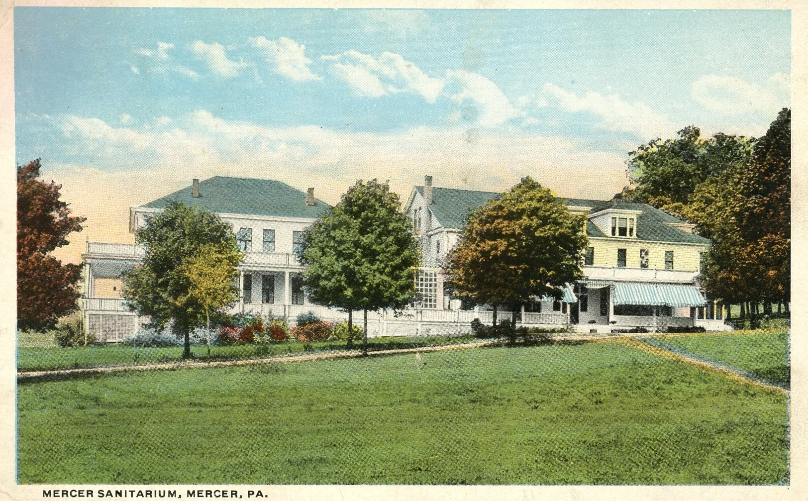 Photograph of the Mercer Sanitarium in Mercer, Pennsylvania, with Victorian-style buildings, surrounded by green trees and a grassy lawn under a partly cloudy sky.