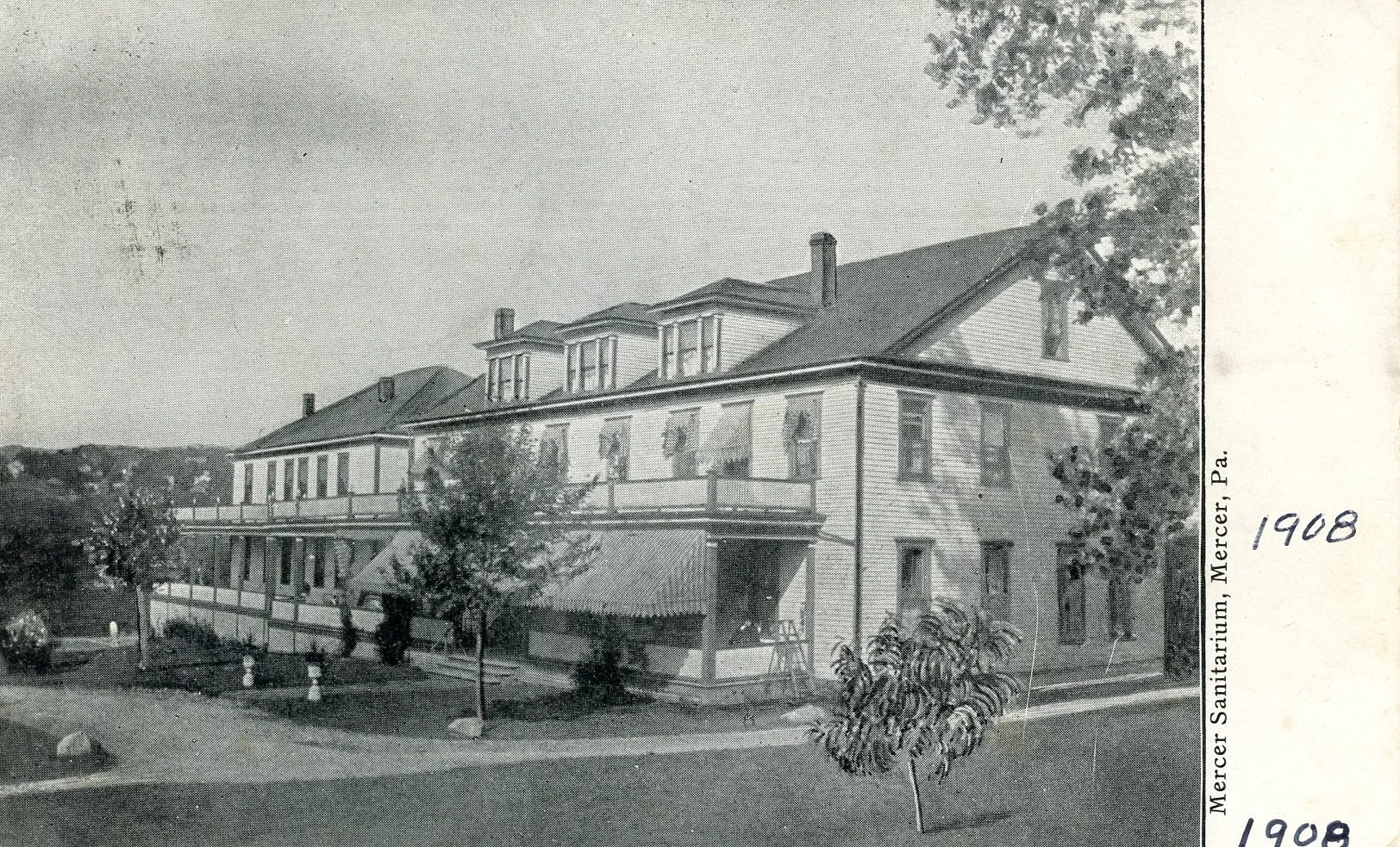 Black and white photograph of a large, multi-story house with a porch, several trees, and a road in the foreground. Text on the right side reads 'Mercer Sanitarium, Mercer, Pa. 1908'.