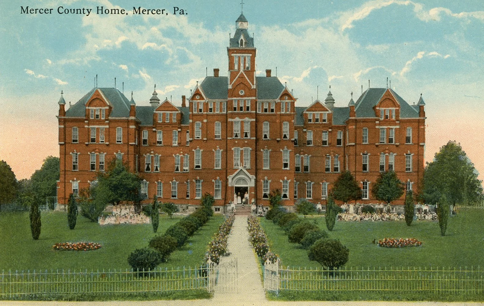 Vintage postcard of Mercer County Home in Mercer, Pennsylvania, showing a large red brick mansion with multiple towers, a well-maintained garden, and a pathway leading to the entrance.