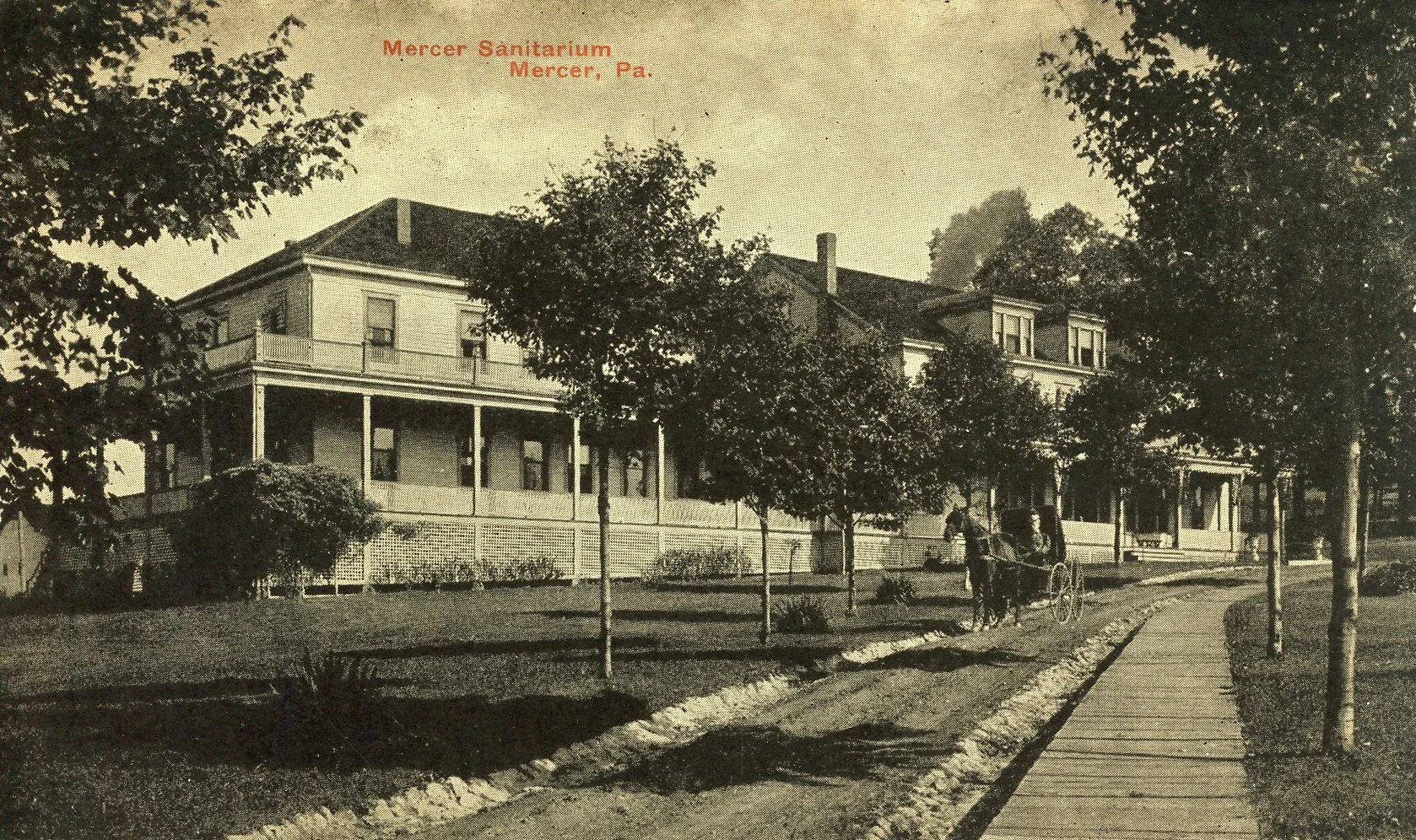 A black and white vintage photograph of Mercer Sanitarium in Mercer, Pennsylvania, showing a large, two-story building with a porch, trees lining the walkway, a horse-drawn carriage on the street, and a sidewalk in front.