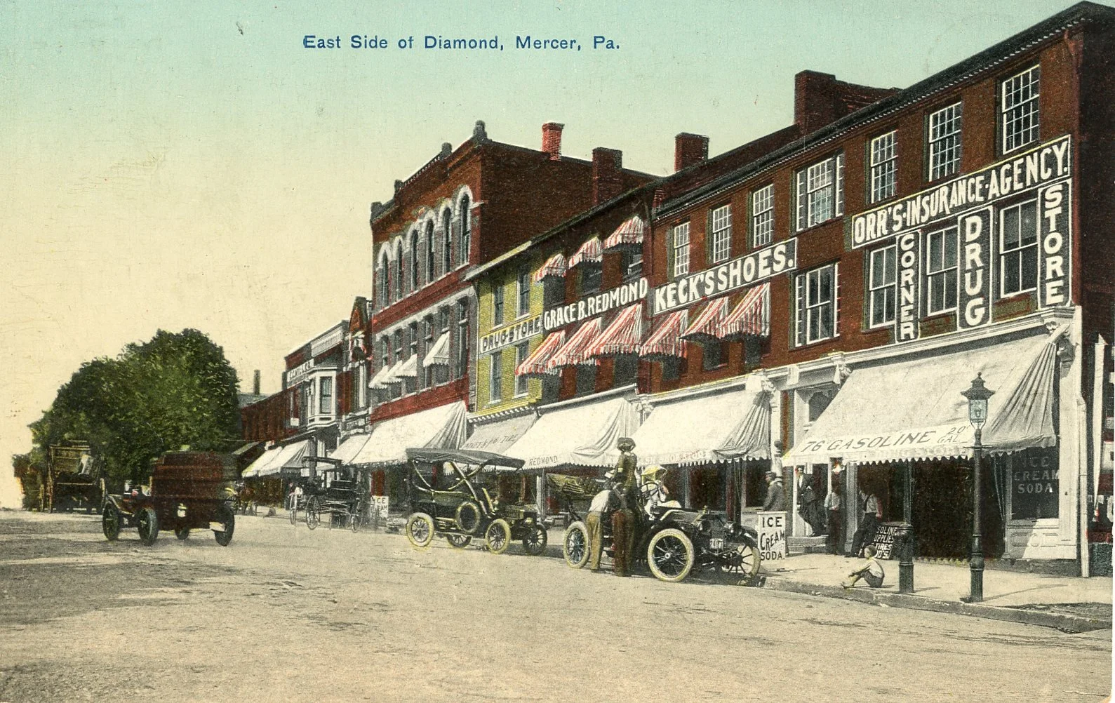 Historical street scene in Mercer, Pennsylvania with brick buildings, storefronts with striped awnings, vintage cars parked along the sidewalk, and people walking or sitting outside. Signs advertise drugstores, insurance agency, shoe store, and ice c