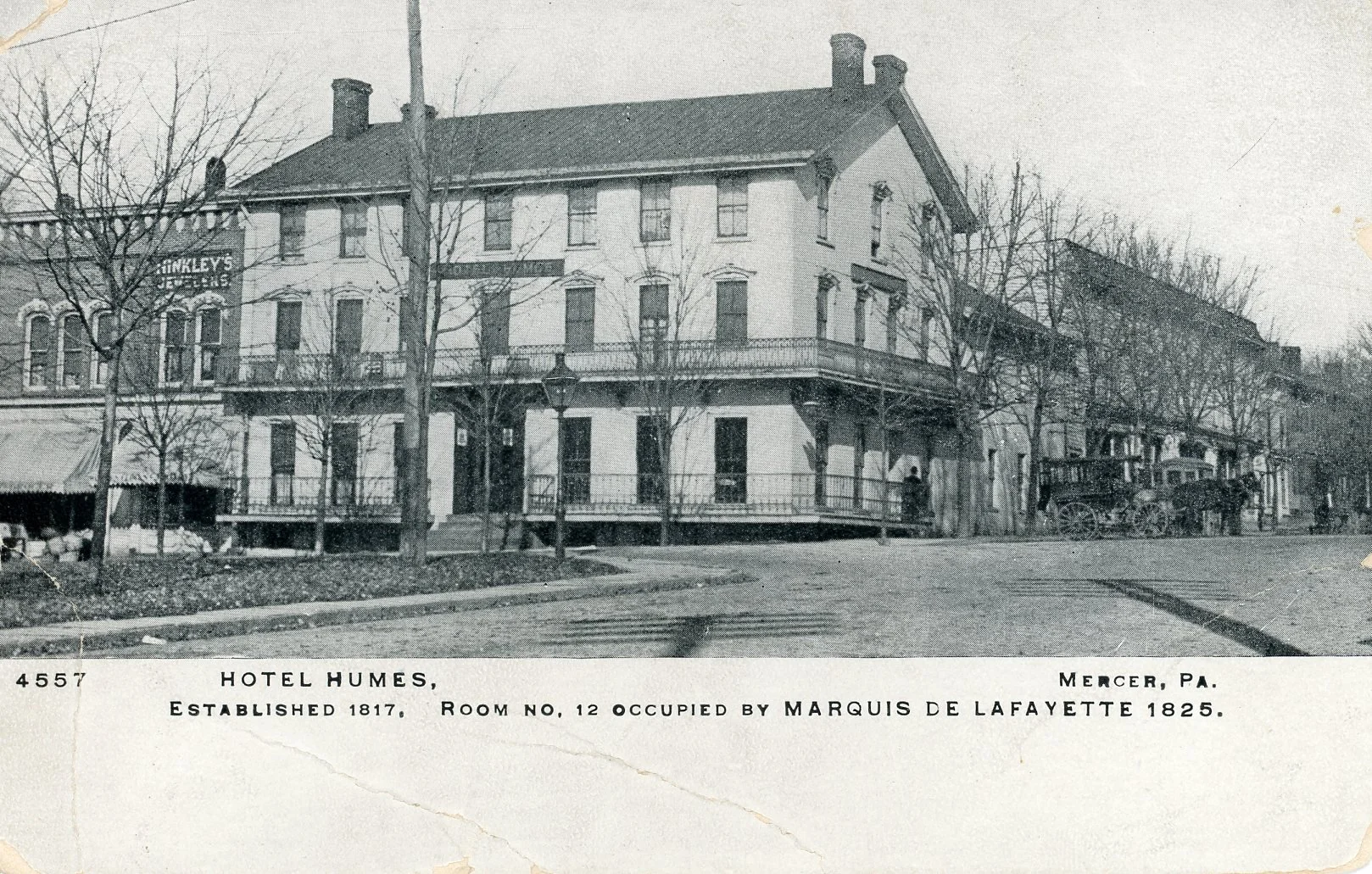 Black and white photo of the Hotel Humes in Mercer, Pennsylvania, built in 1817, with a porch, trees, and a vintage carriage parked in front.