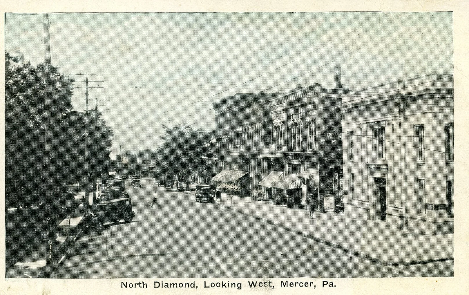 Black and white photo of a small town street with buildings, parked cars, and a few pedestrians, titled 'North Diamond, Looking West, Mercer, Pa.'