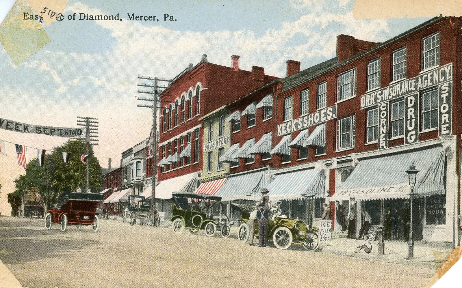 A vintage street scene in Mercer, Pennsylvania, featuring brick buildings with signage for stores like a drug store and shoe store, horse-drawn carriages, and pedestrians. The scene includes a banner advertising an event and flags decorating the stre