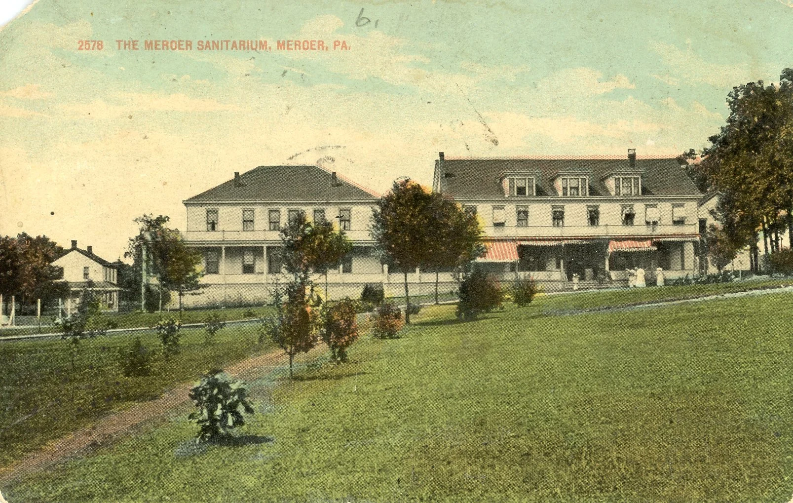 Vintage color postcard of The Mercer Sanitarium in Meroer, Pennsylvania, showing a large two-story building with a porch, surrounded by a grassy area with trees, and smaller houses nearby.