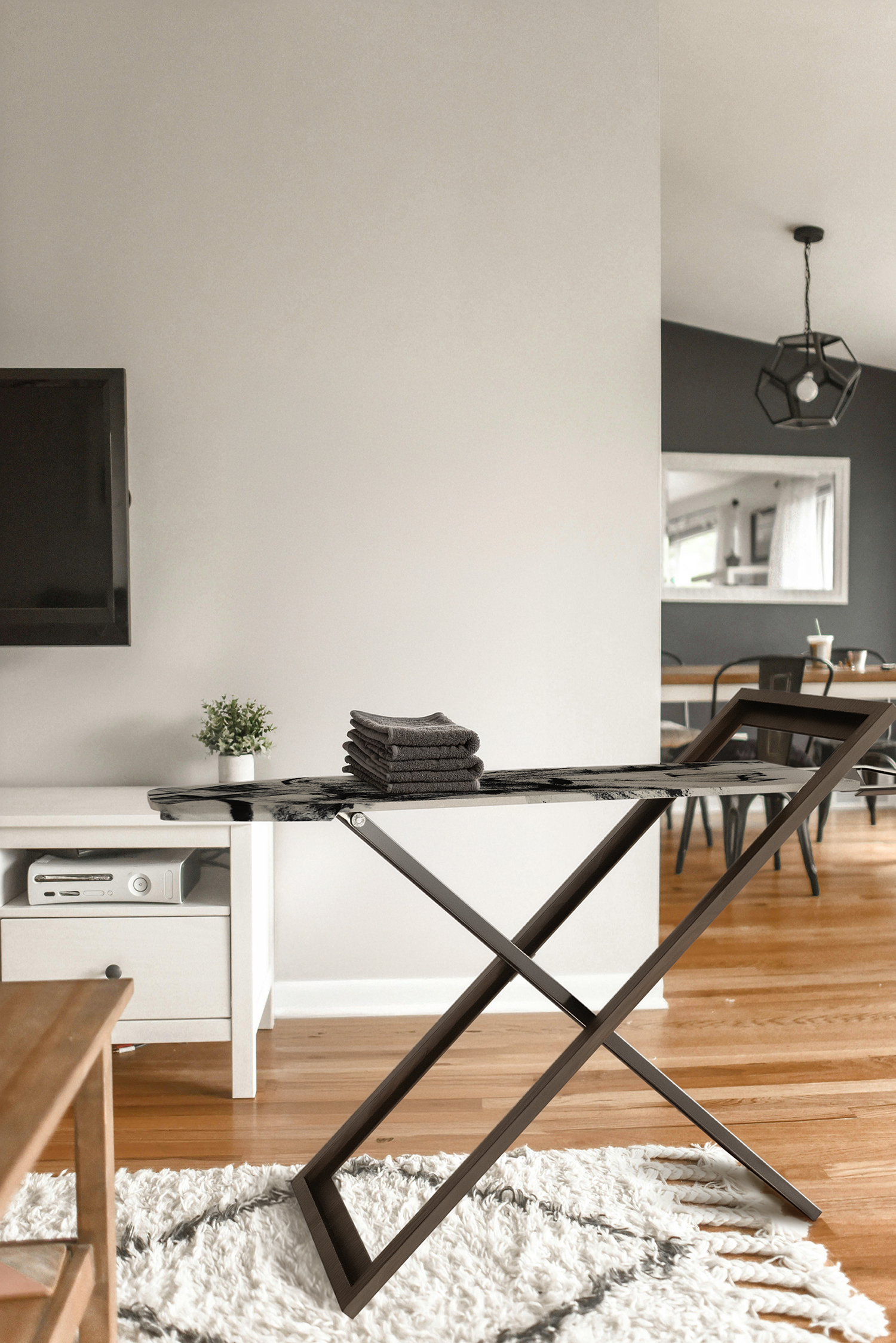 Moderner Wohnraum mit weißen Wänden, Holzboden, TV und dem innovativen IRONY Bügelbrett im aufgeklappten Zustand. Das Bügelbrett dass sich nicht verstecken muss.