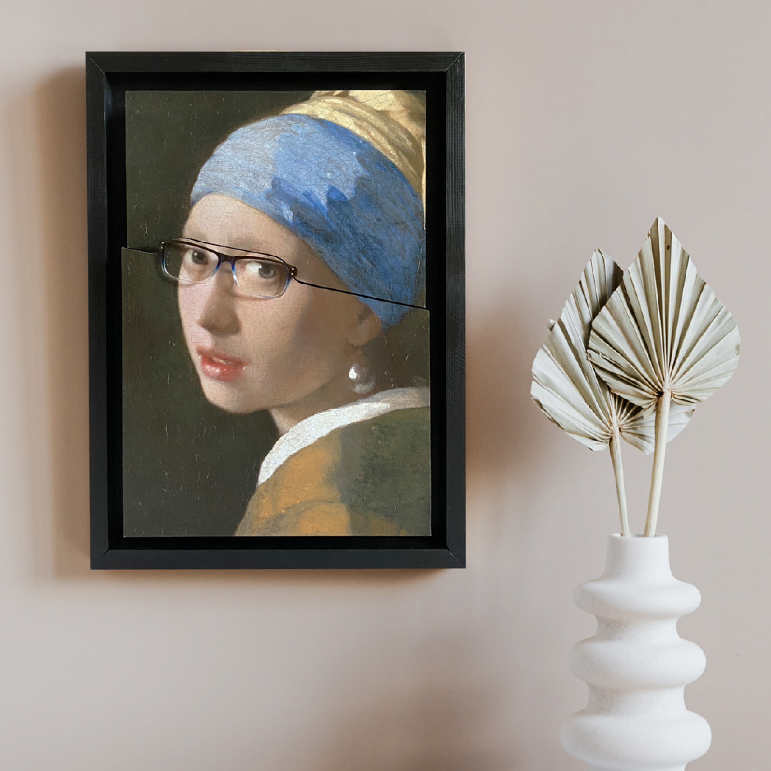 Das Fame Frame - der clevere Brillenhalter als Version des "Mädchen mit dem Perlenohrring" von Jan Vermeer neben einer weißen Vase mit getrockneten Blättern