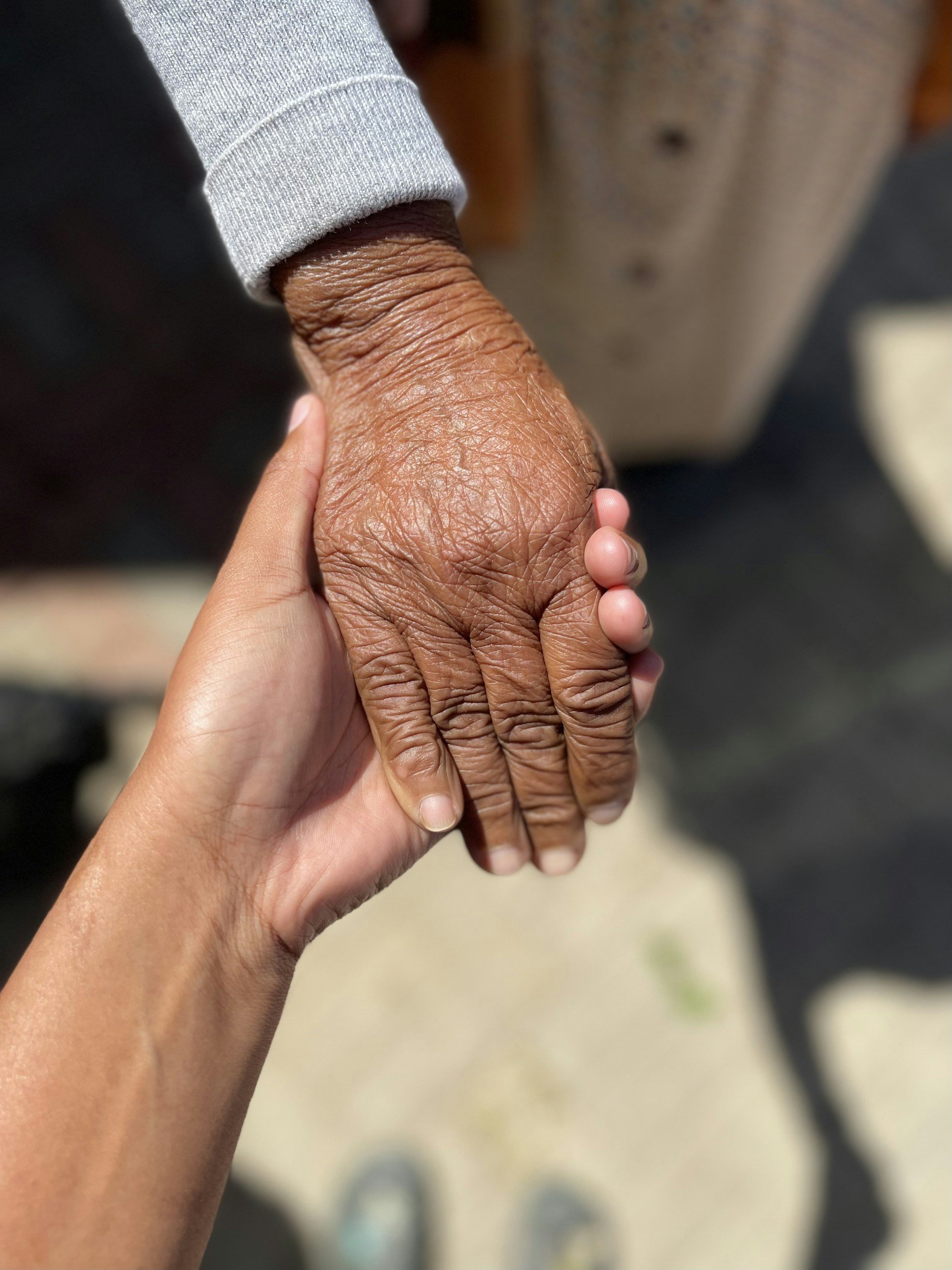 A young person's hand holding an elderly person's hand outdoors.