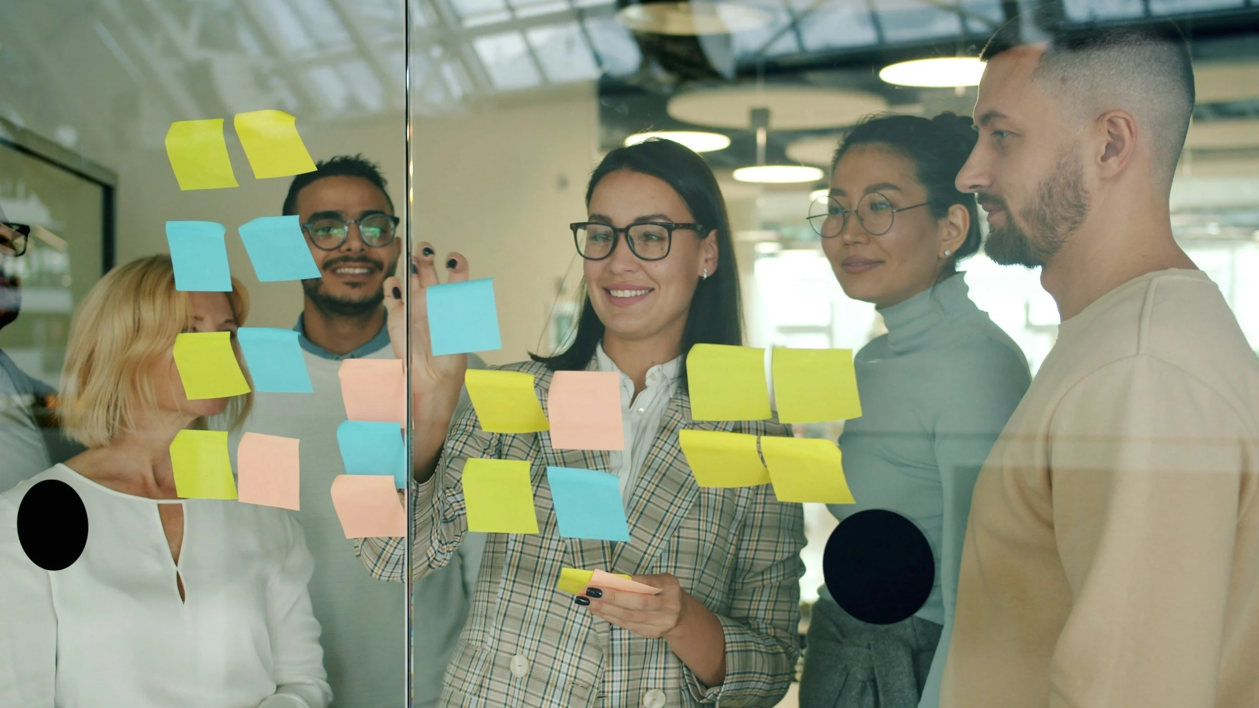 Group of individuals using sticky notes on a window to organize information for planning.