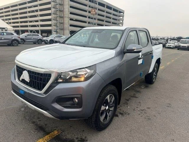 Gray pickup truck parked in lot with new car covers on the hood and doors, with a multi-story parking garage in background.