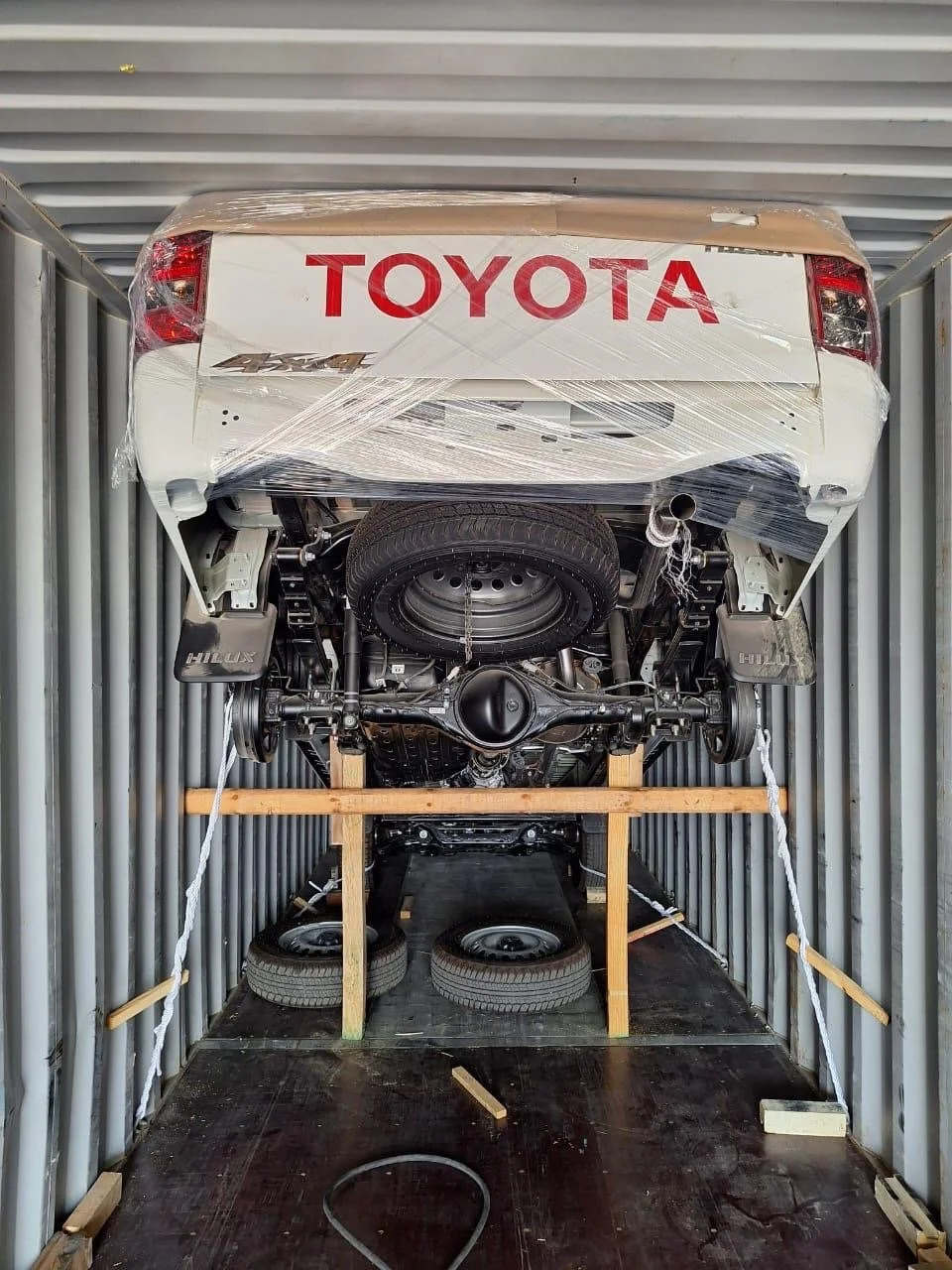 Rear view of a Toyota car in a shipping container, secured with wooden blocks and straps, with the Toyota logo visible on the back of the car.