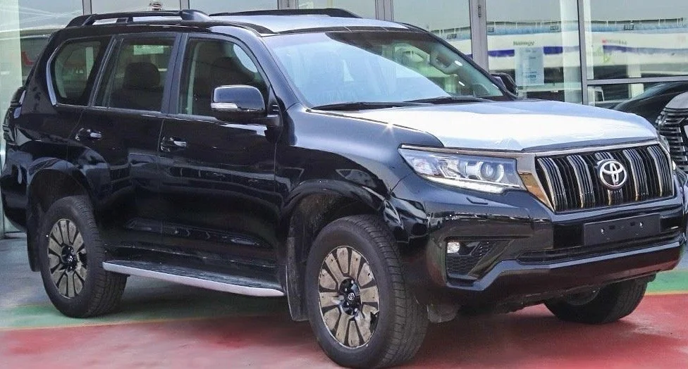 A black Toyota SUV parked outdoors, possibly at a dealership, with rain on the ground and other vehicles visible in the background.