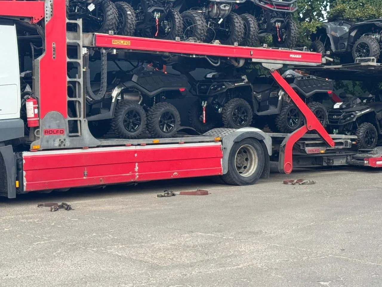 A red car hauler truck loaded with small all-terrain vehicles parked on an asphalt surface during daytime.