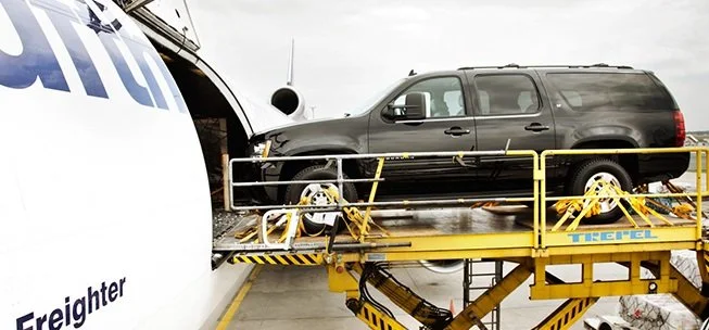 Black SUV being loaded onto an airplane cargo hold using a yellow cargo lift.