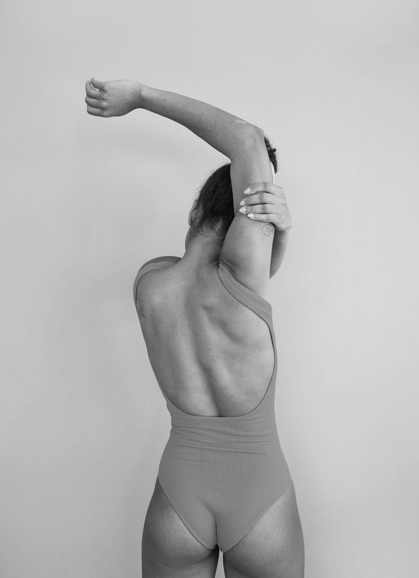 A person in a swimsuit stretching with one arm over their head, seen from the back.