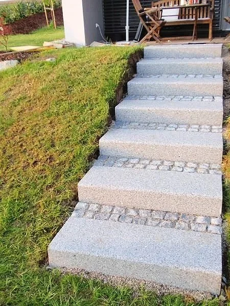 Stufen aus Beton im Garten vor einem Haus mit Terrasse.
