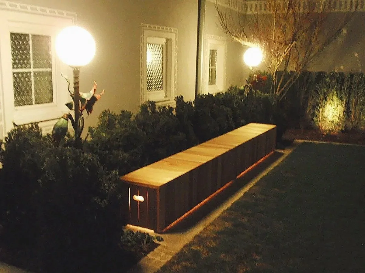 Außenansicht mit einer beleuchteten Laterne, Büschen und einem Windlicht, bei Nacht.